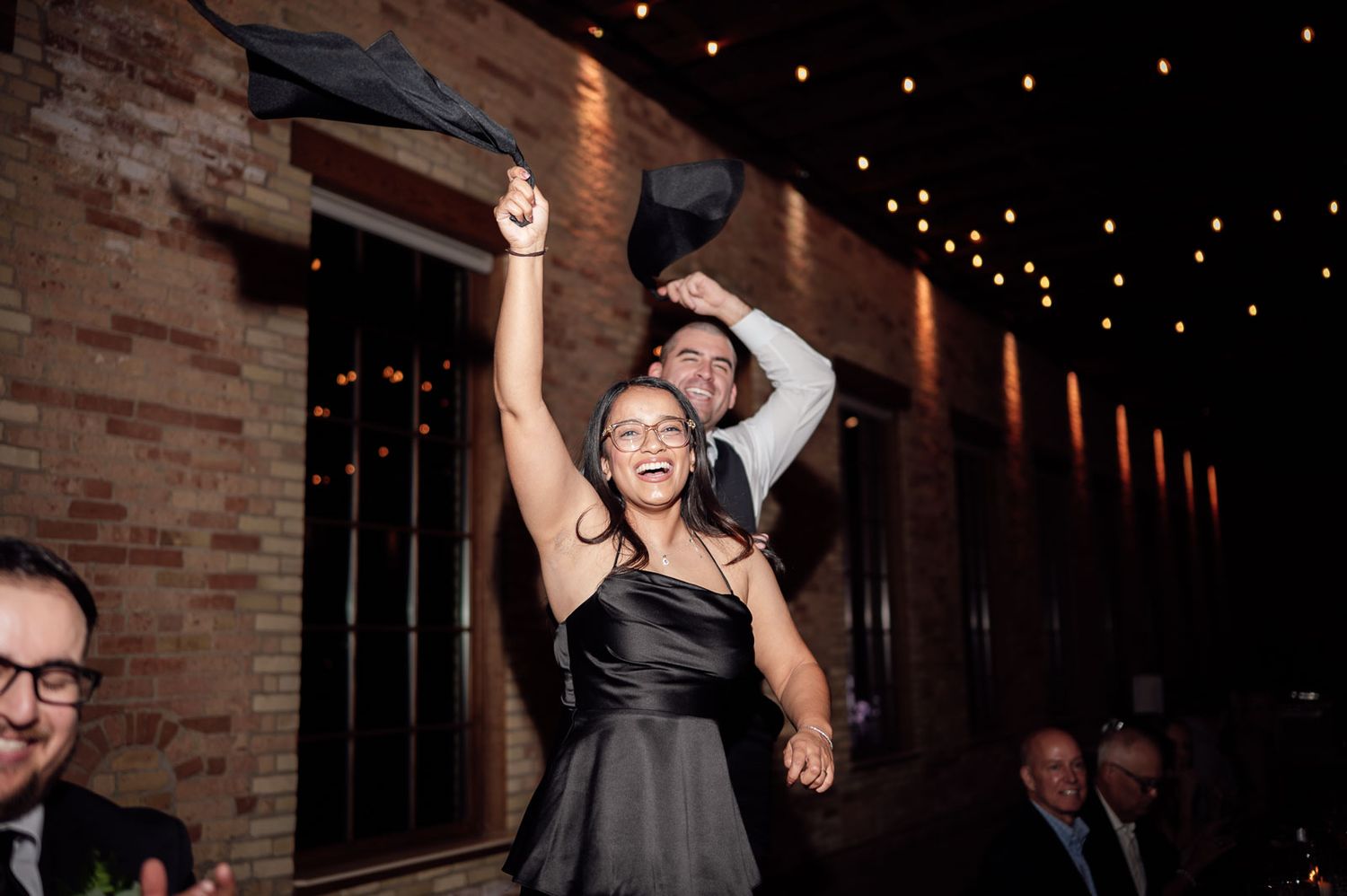Excited wedding guest in black dress celebrates on the dance floor at a festive wedding reception.