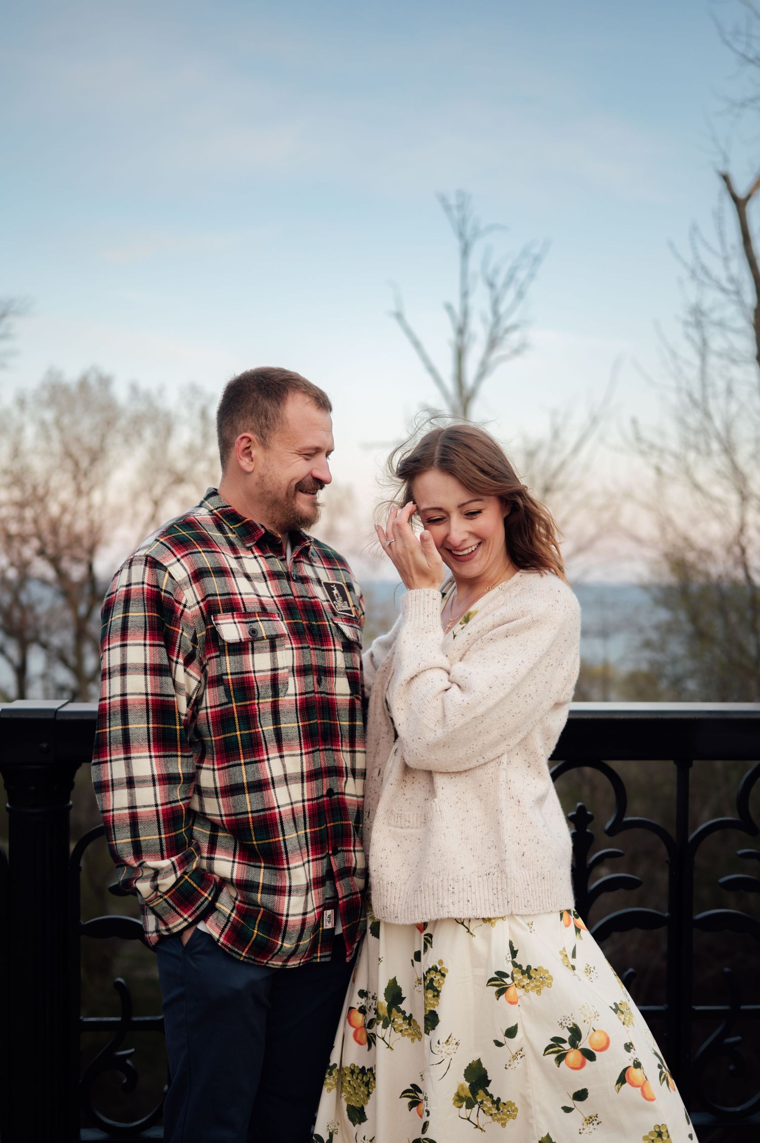 Smiling couple sharing a joyful moment outdoors on a balcony with bare winter trees in the background.
