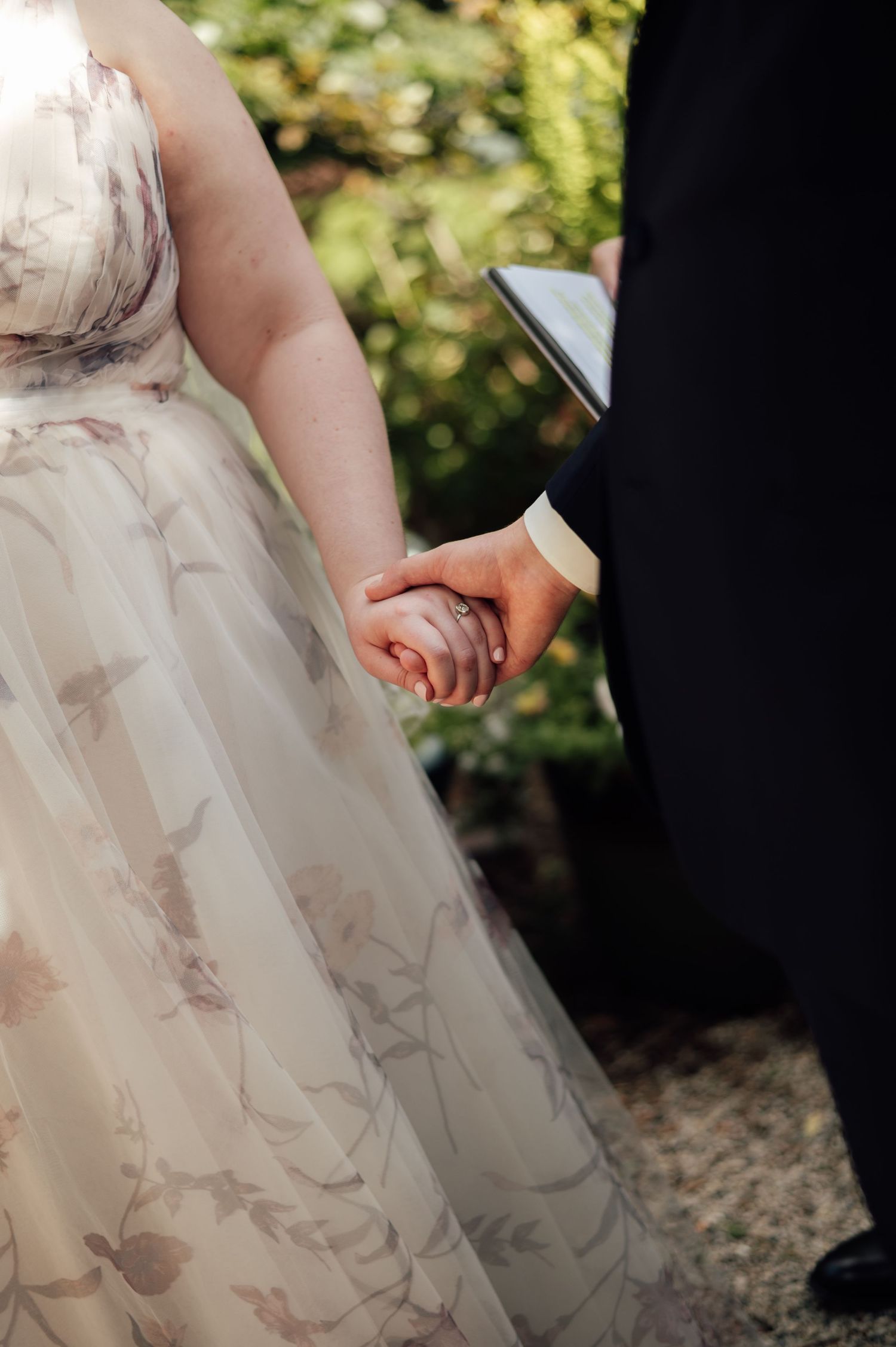Bride and groom holding hands during outdoor wedding ceremony, bride wearing floral tulle gown.