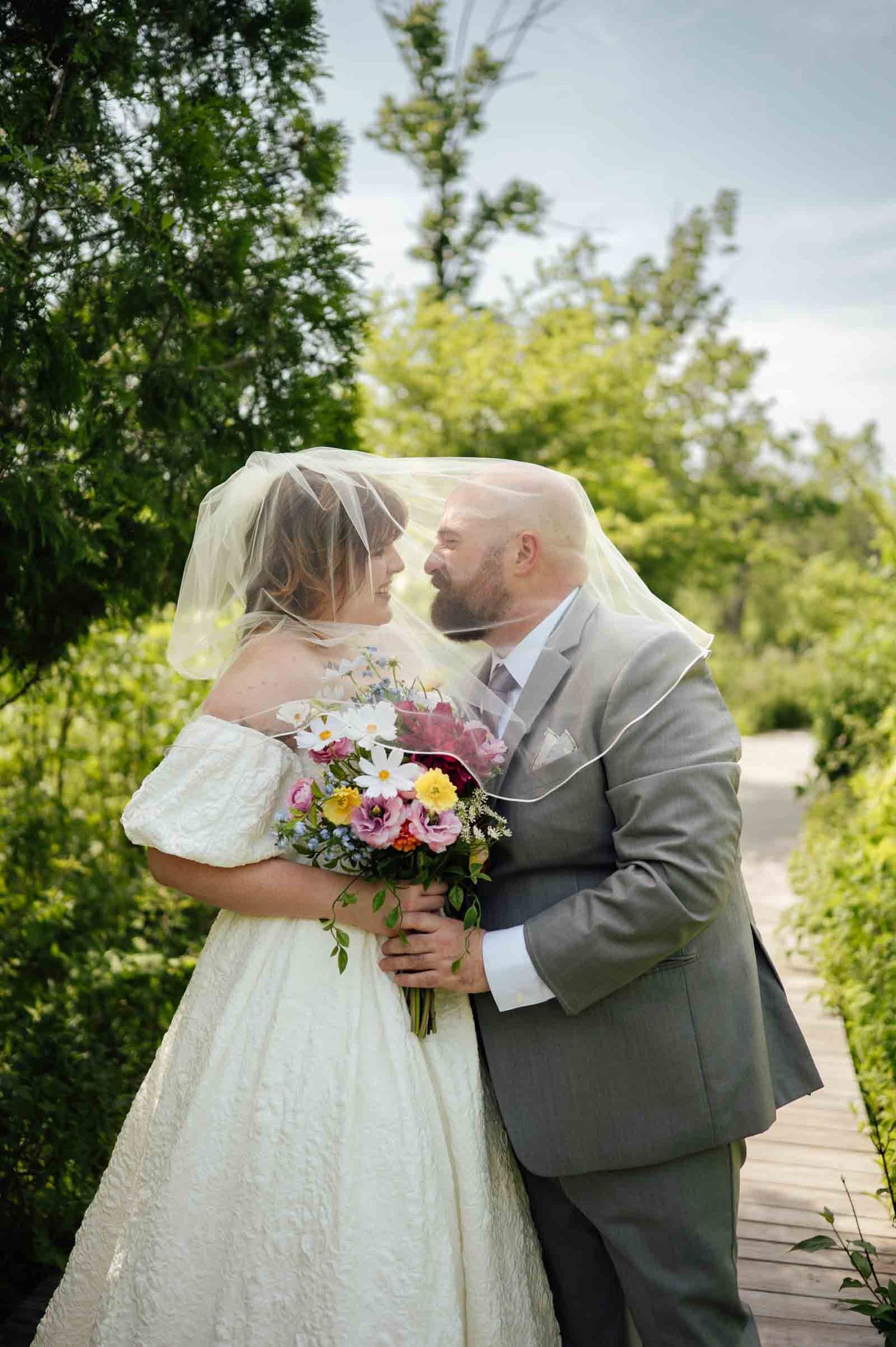 Bride and groom sharing romantic moment under veil in lush garden setting.