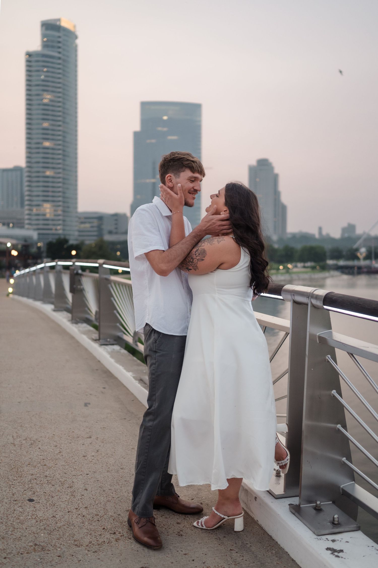 Couple sharing a tender moment on a Milwaukee bridge at dusk with urban skyline backdrop.