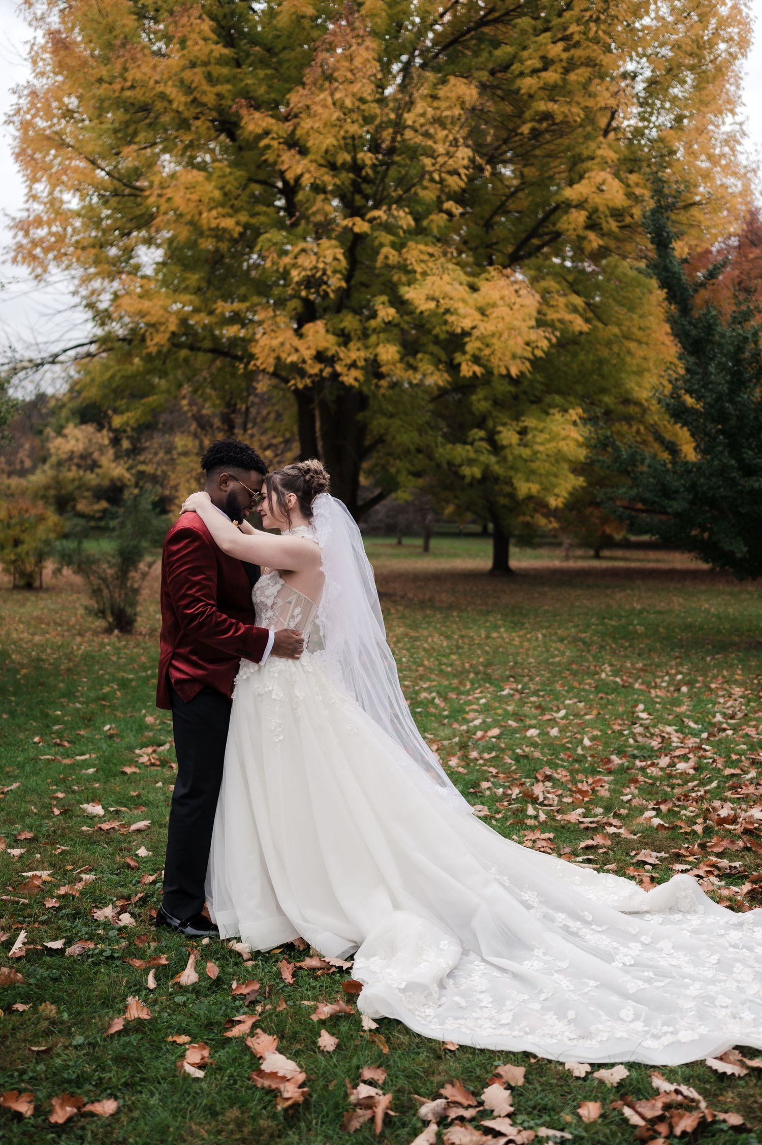 A wedding couple poses together on fallen leaves with beautiful autumn trees creating a romantic backdrop.