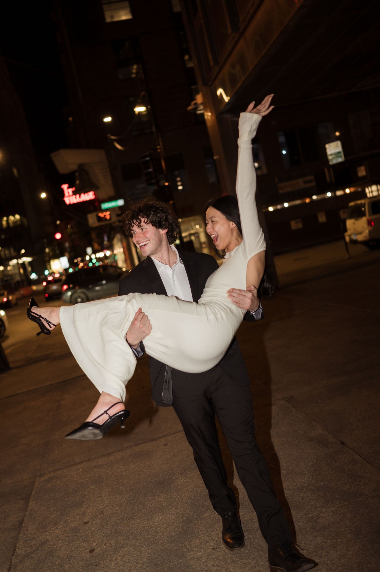 Groom joyfully carrying bride in his arms on a Chicago street at night during their wedding celebration.