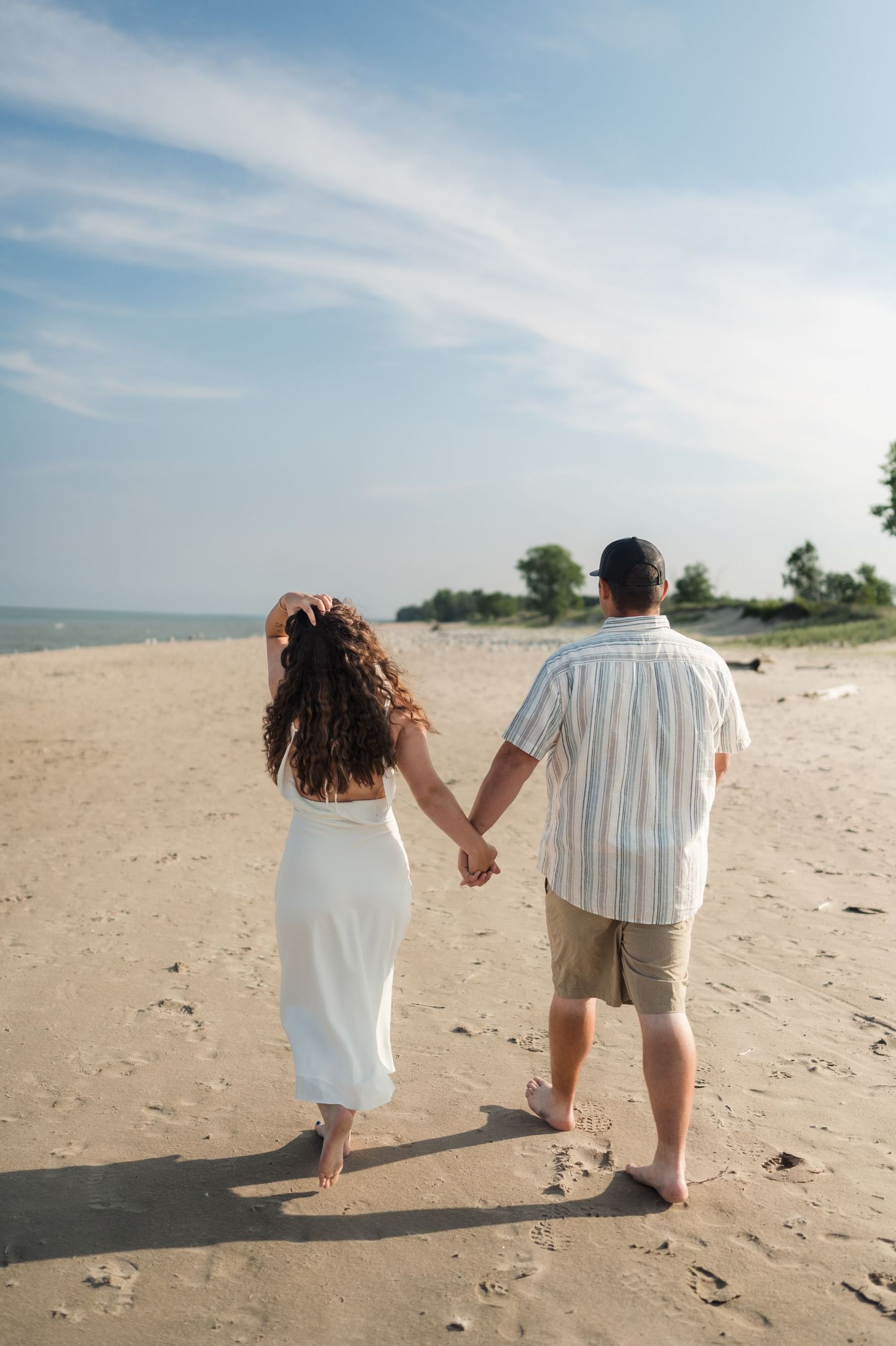 A couple walking hand in hand along a serene beach on a sunny day with blue skies.