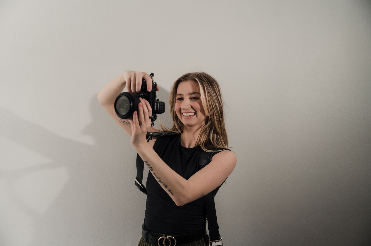 Smiling female photographer holding a professional camera against a light gray studio background.