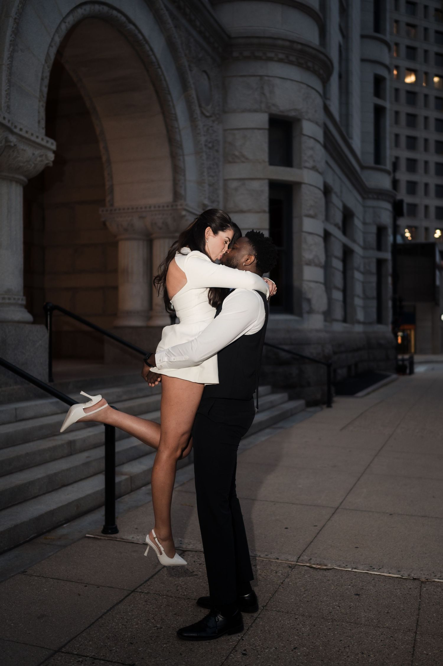 Romantic couple sharing a passionate embrace and kiss outside a historic stone building at night.