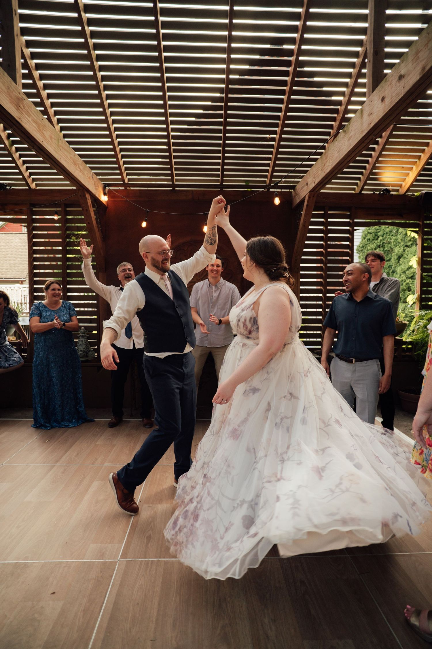 Bride and groom share first dance, spinning joyfully in floral gown at elegant indoor wedding reception.