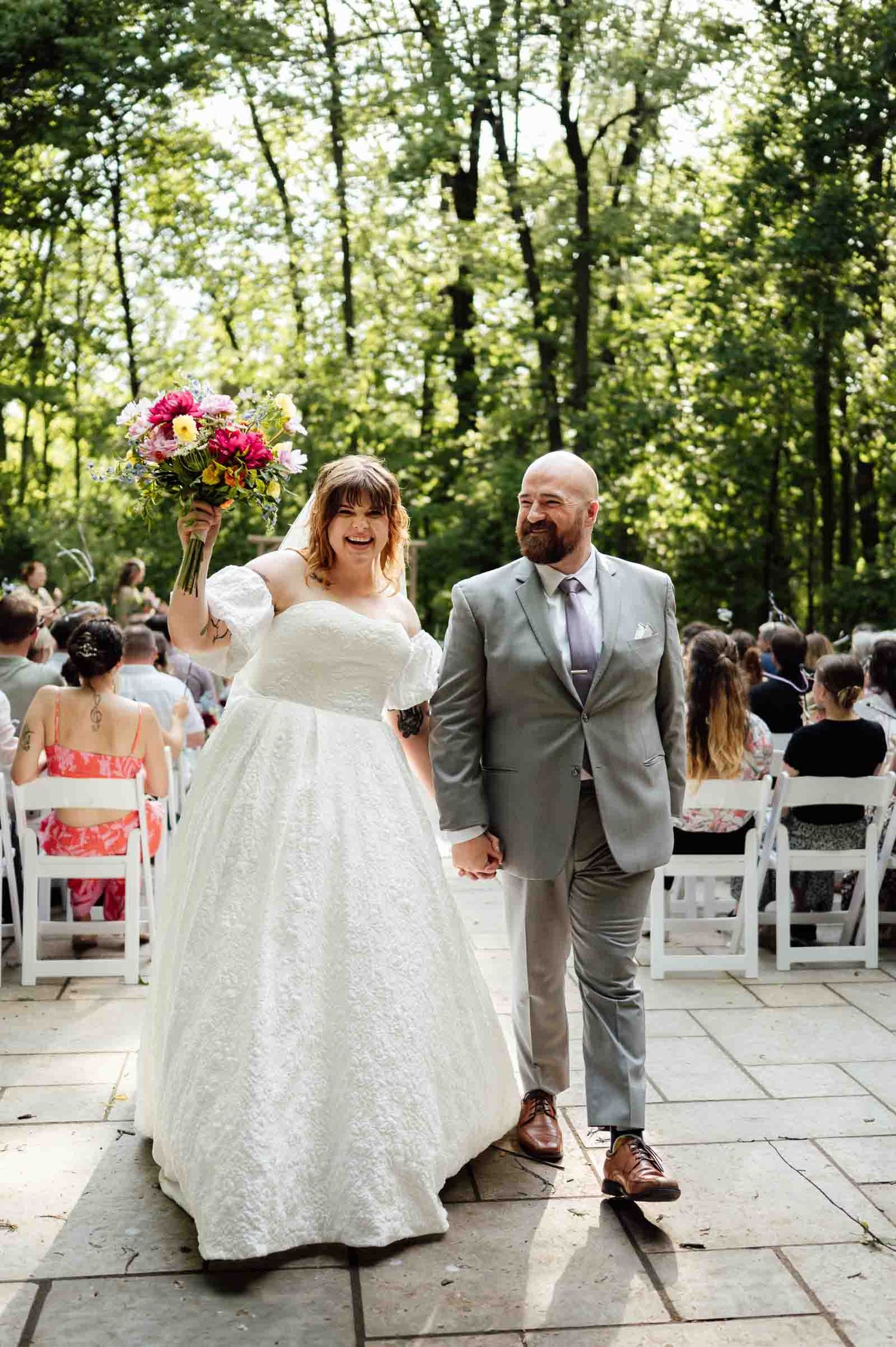 Newlyweds celebrating with raised bouquet while walking back down ceremony aisle.