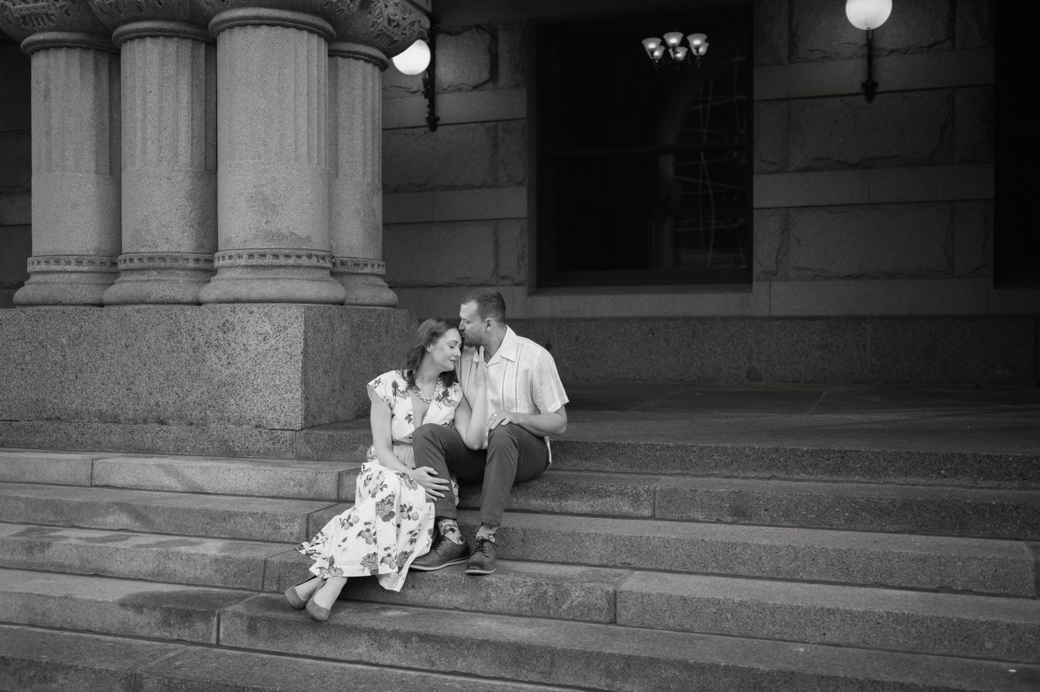 Black and white photo of couple sitting closely together on stone steps of a classic building.