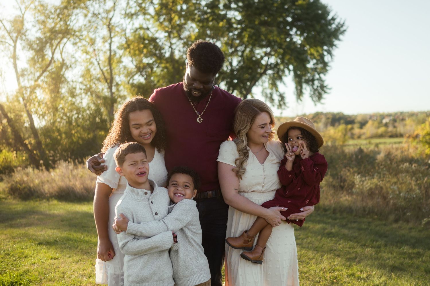 Happy blended family of six posing together in golden hour sunlit outdoor field setting.