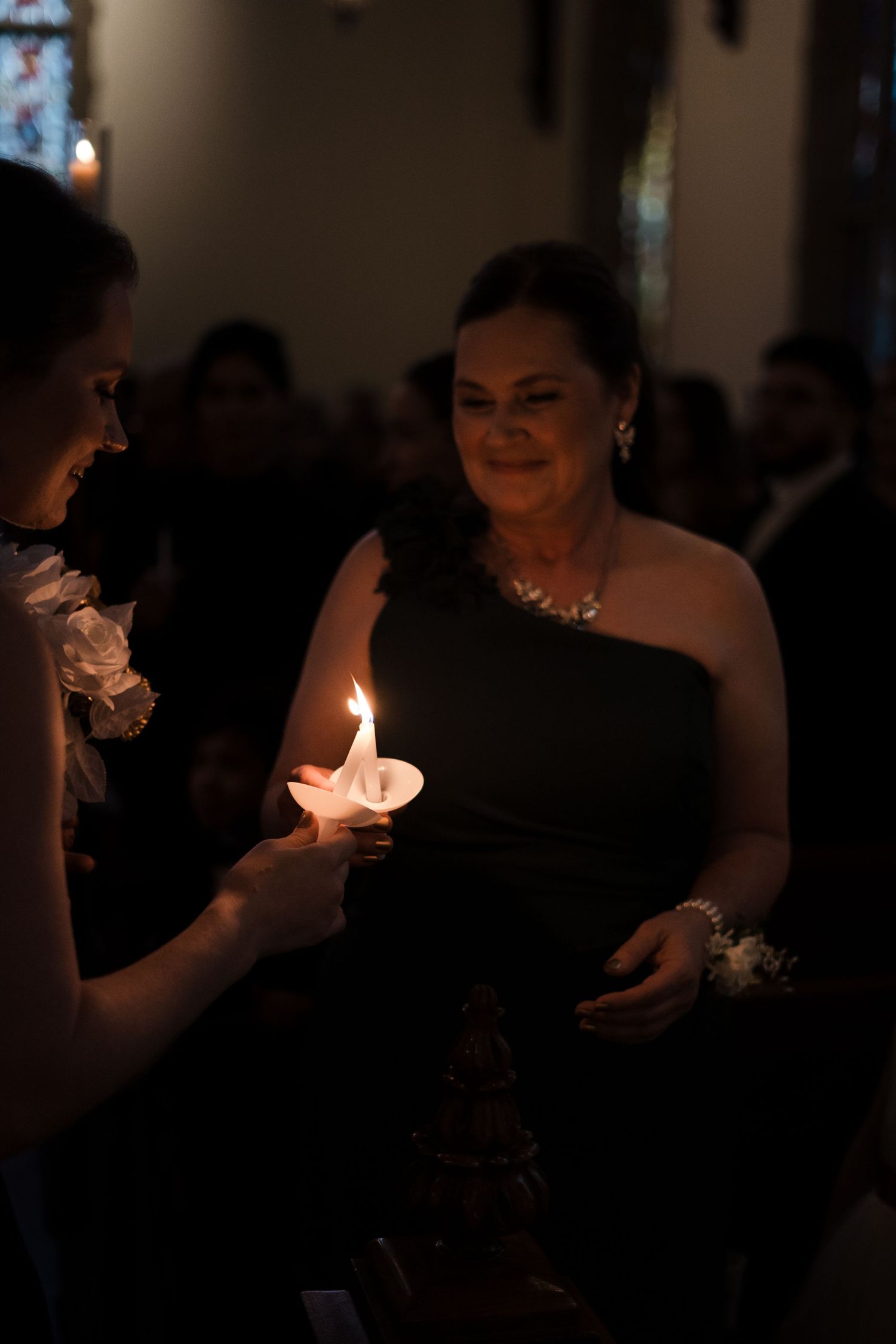 Wedding guests hold lit candles in a darkened church during an evening ceremony.
