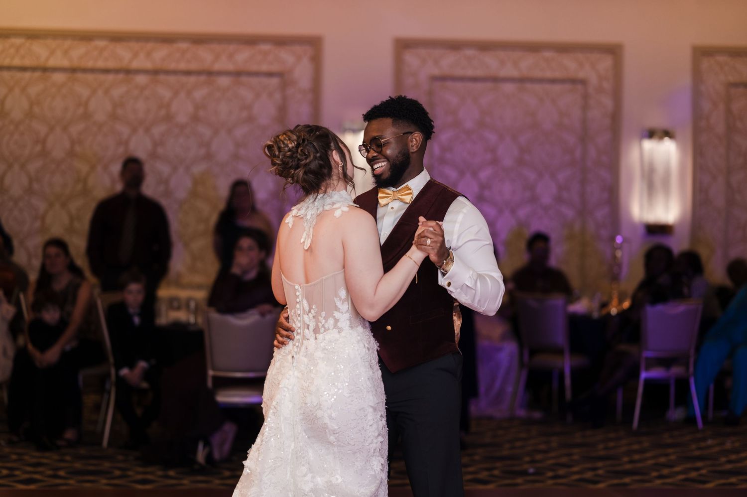 A couple shares a romantic dance together at their wedding reception with purple lighting in the background.