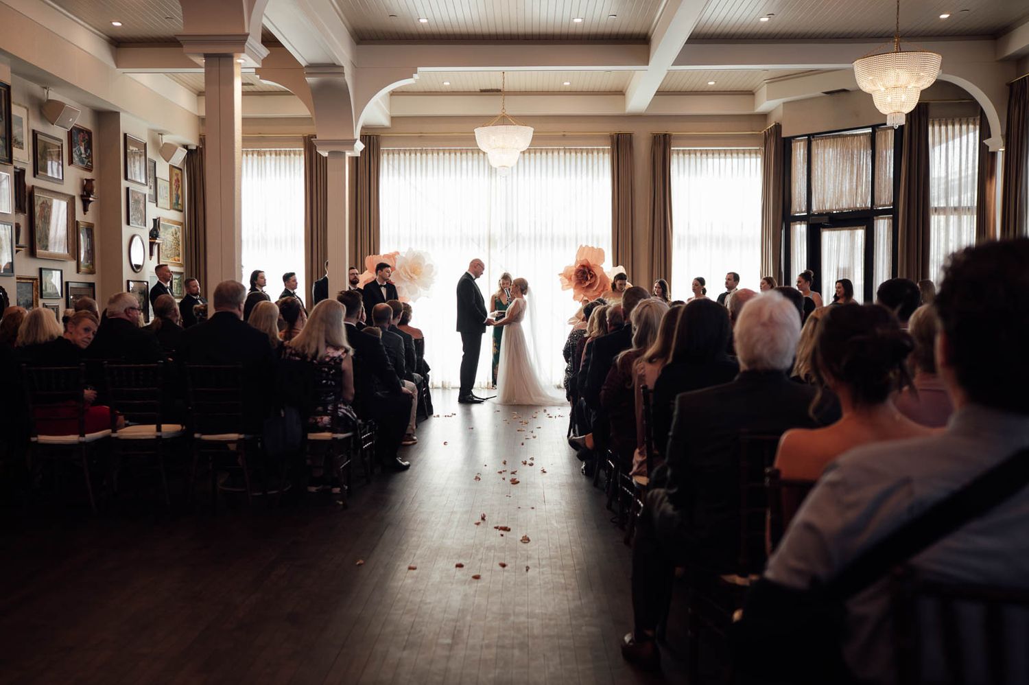 Wedding ceremony in elegant venue with guests seated as couple exchanges vows at floral altar.