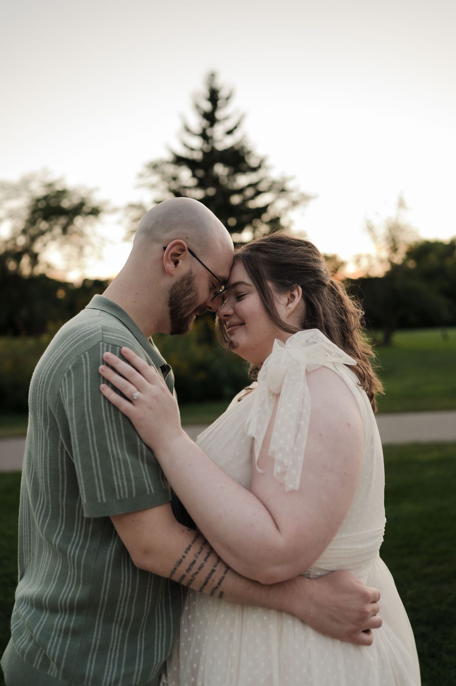 Couple sharing an intimate forehead-to-forehead embrace at golden hour in a lush green park setting.