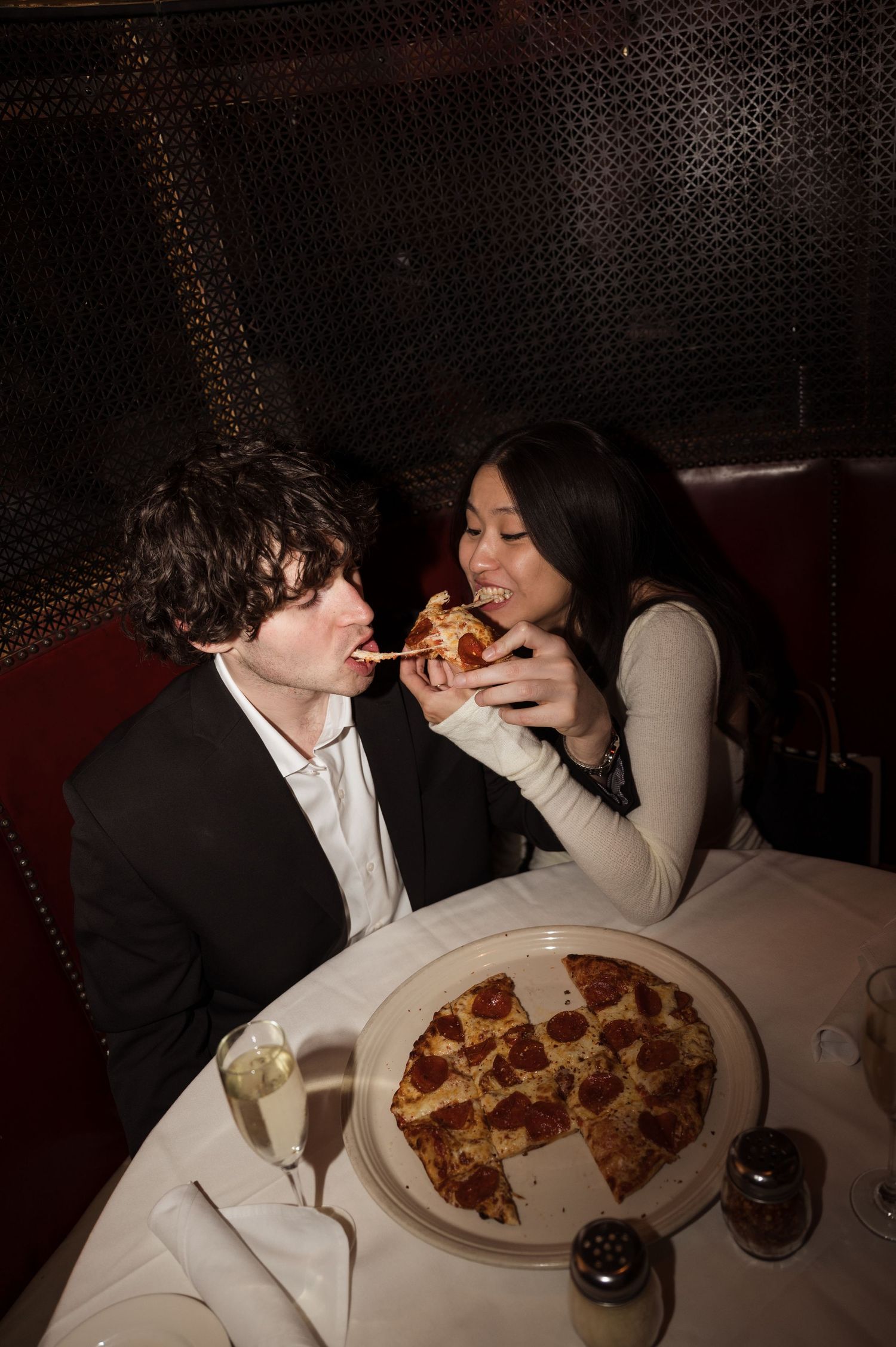 Bride feeding groom a slice of pepperoni pizza at a romantic Chicago restaurant with champagne glasses nearby.