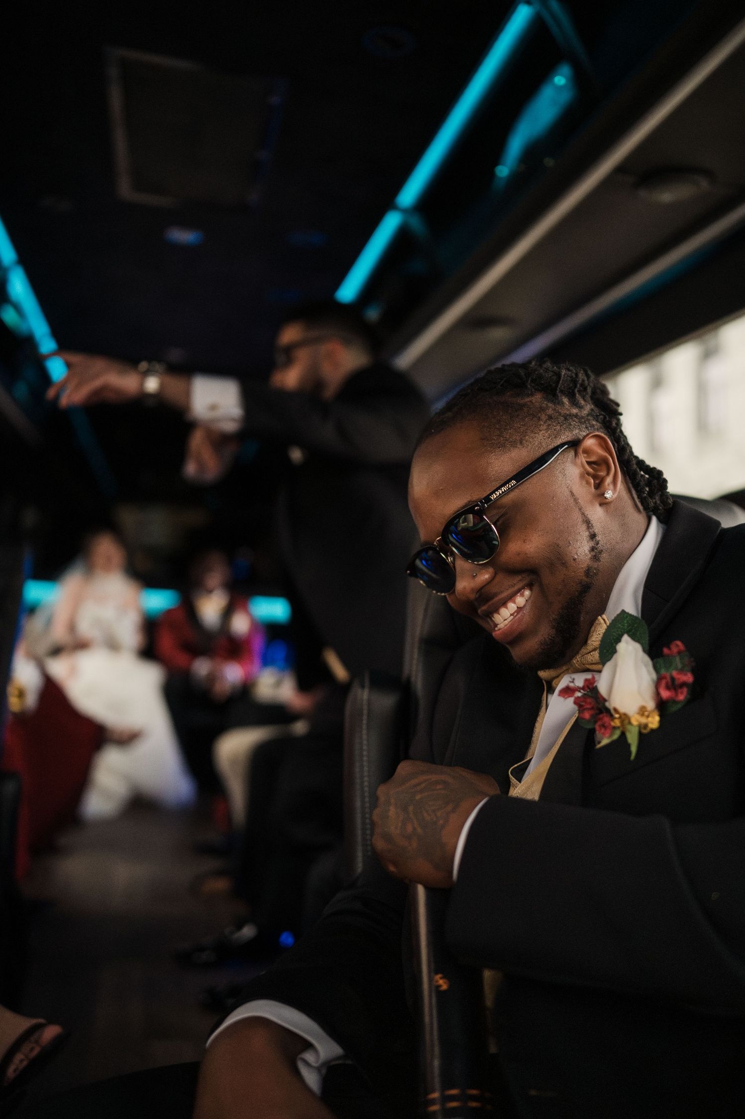 A performer in sunglasses and formal attire smiles while singing into a microphone during an indoor event.
