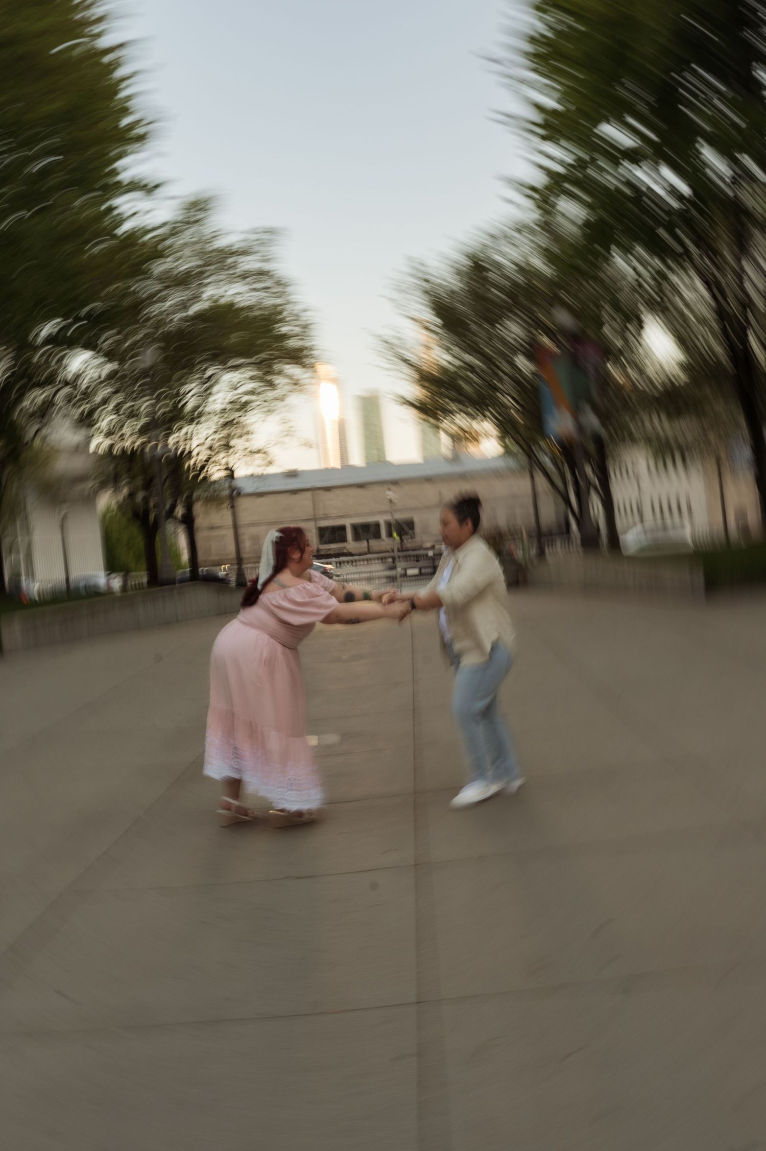 Couple spinning and dancing outdoors with motion blur effect in urban park setting.