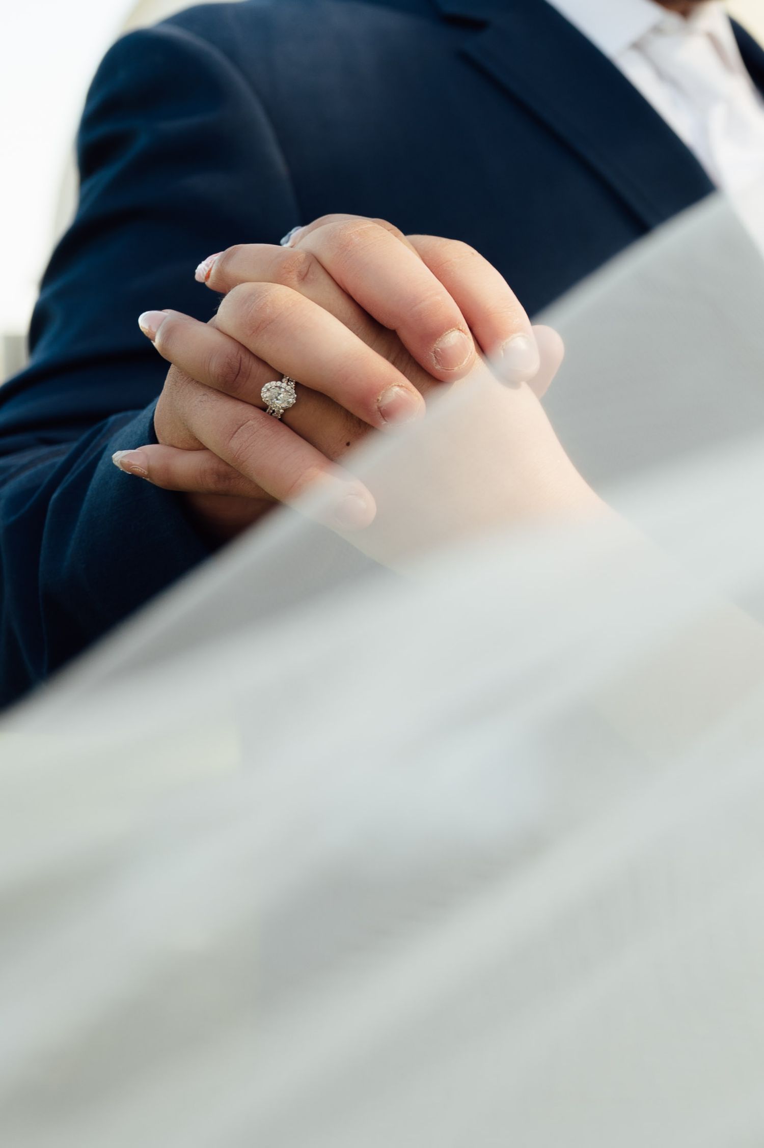 Close-up of bride and grooms clasped hands showing a stunning diamond engagement ring.