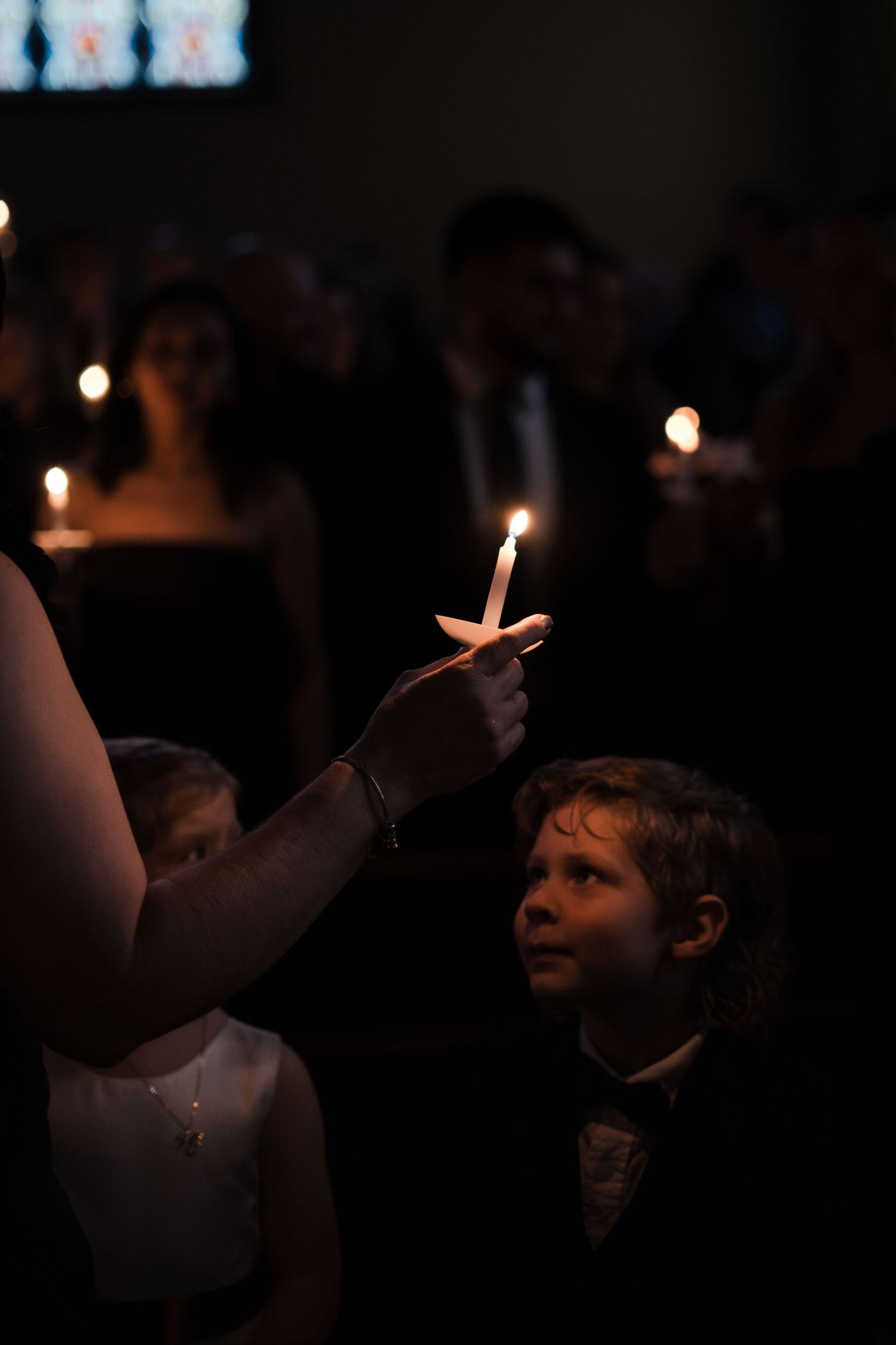 A candlelight vigil shows silhouettes of people holding glowing candles in a darkened room.