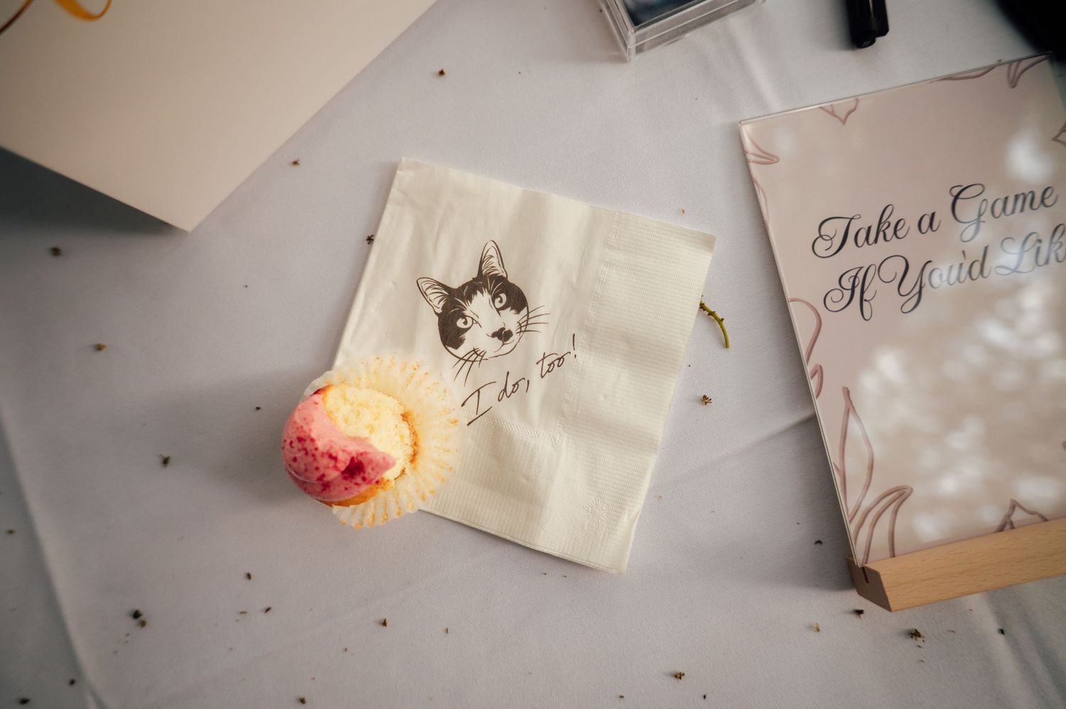 Wedding cupcake next to a cat-themed paper bag reading I do too on a decorated table with a Take a Game sign.