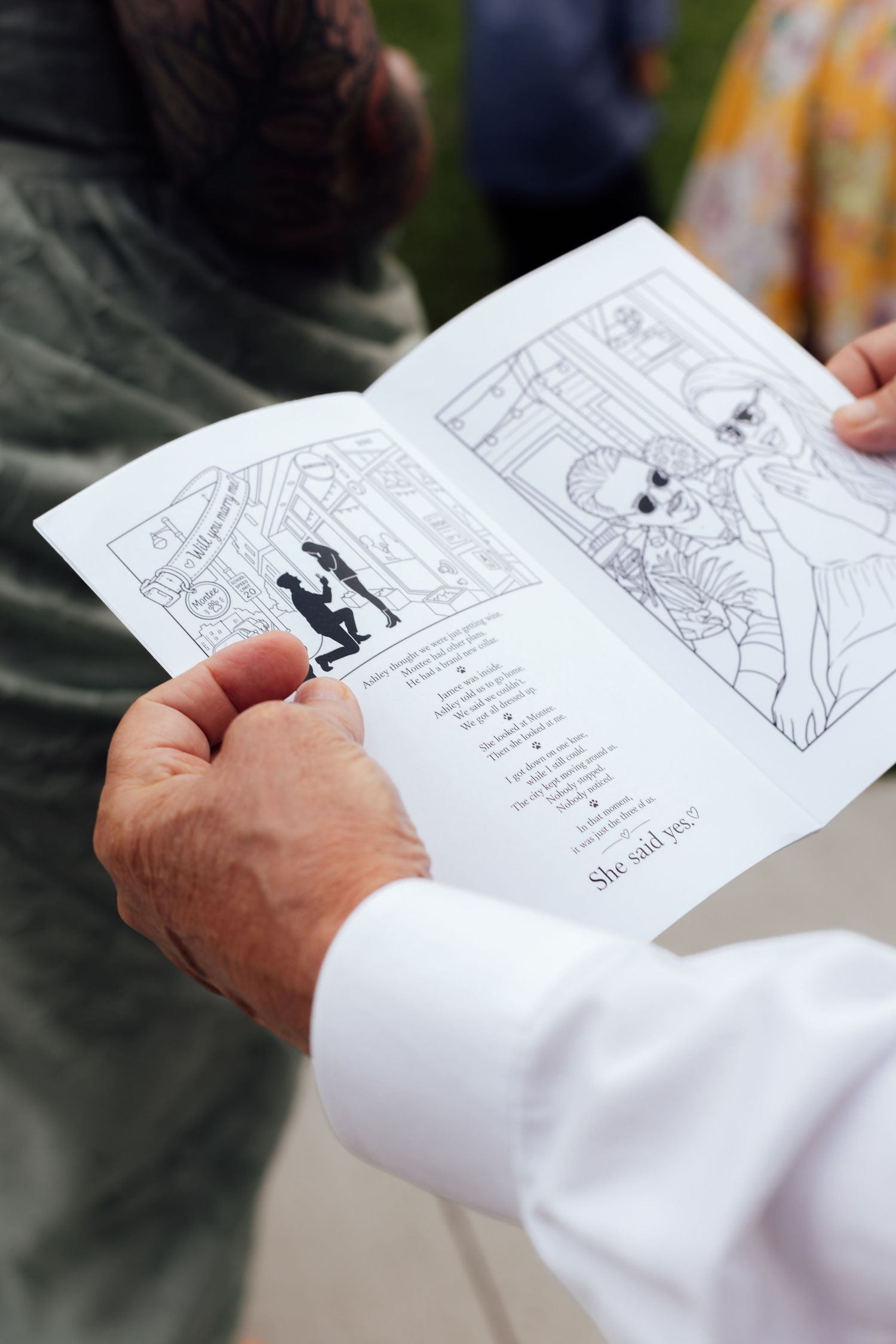 Person holding open wedding program booklet with illustrated black and white drawings and text reading She said yes.
