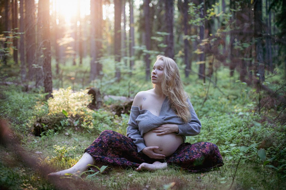 Raskaana oleva nainen istumassa metsässä, rauhallinen ja herkkä hetki luonnon keskellä