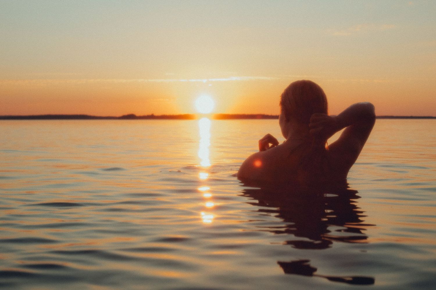 Nainen vedessä auringonlaskussa, siluetti ja rauhallinen, merkityksellinen hetki