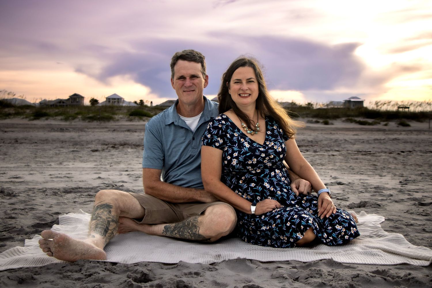 A couple posing for a couple's portrait at St. Augustine beach during the golden sunset hour sitting next to each other.