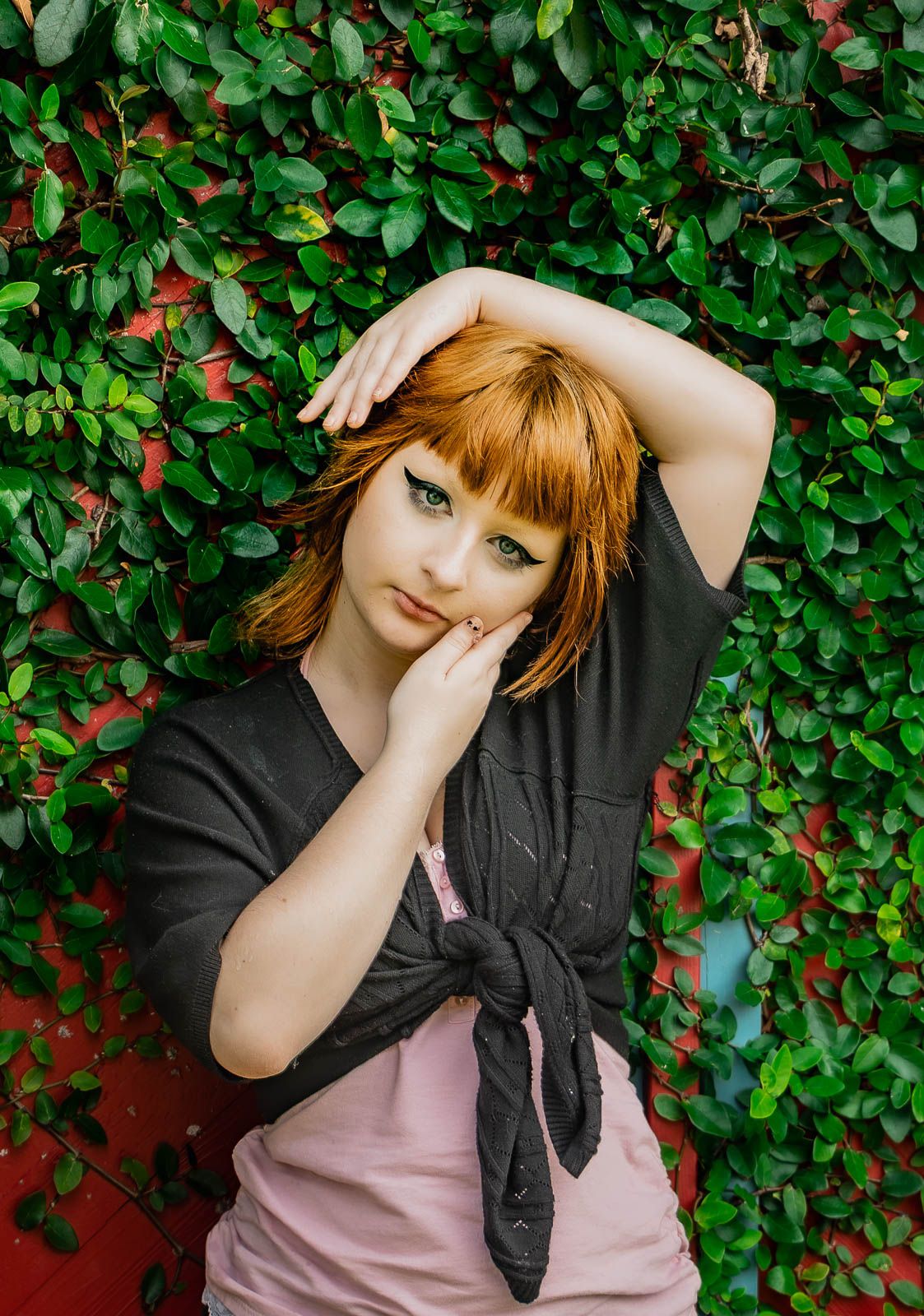 Girl poses up against a red door with green ivy posing for her portrait session in Jacksonville, Florida.