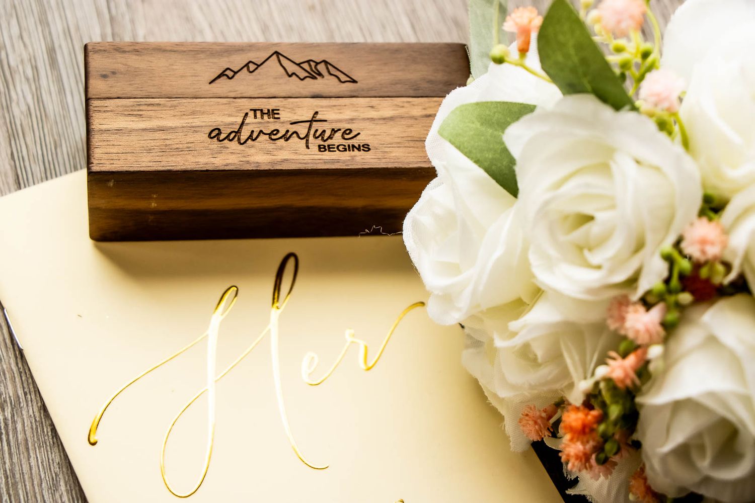 Wooden adventure begins box with white roses bouquet on gold calligraphy wedding stationery.