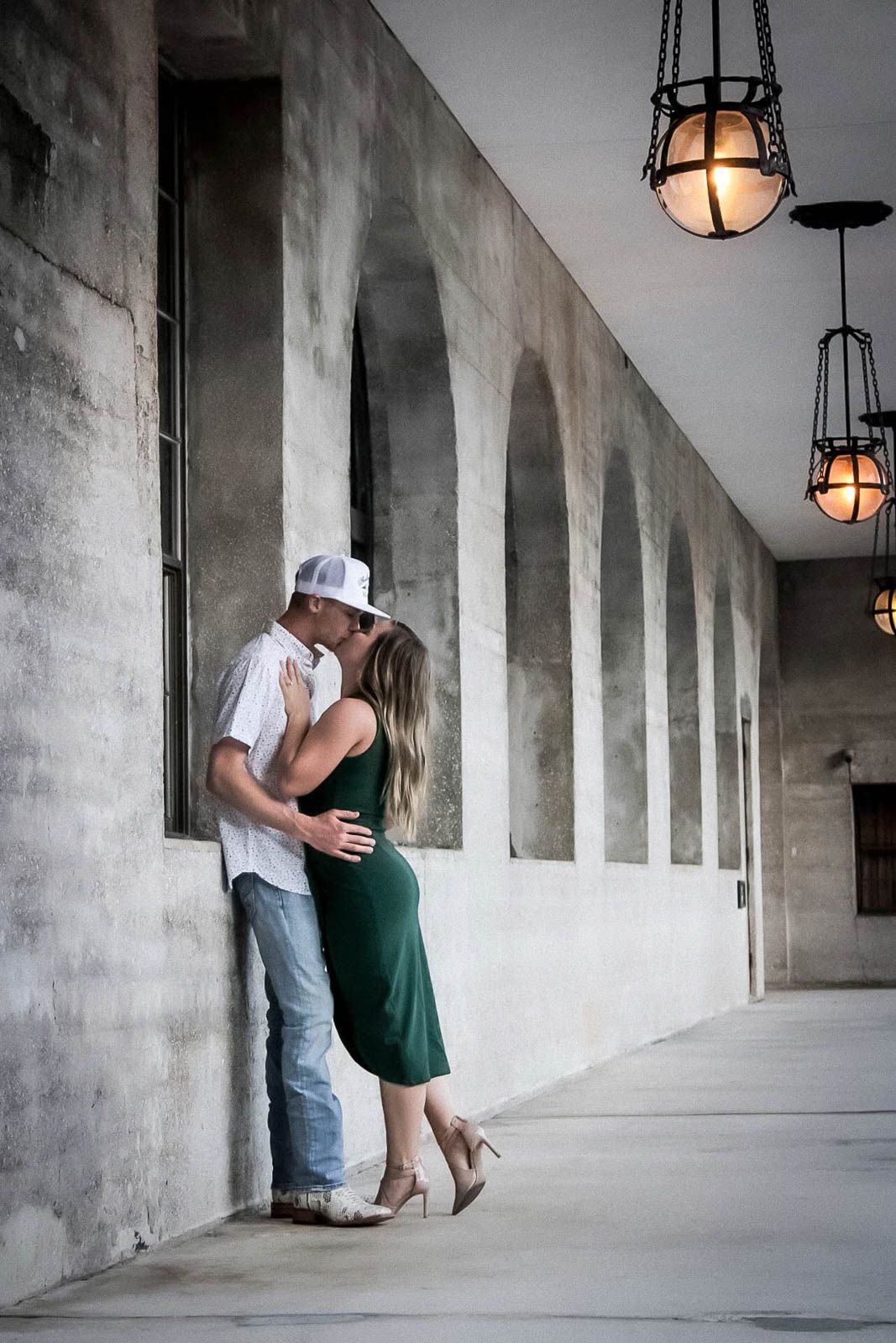 Couple sharing a romantic kiss in an arched corridor with vintage industrial pendant lights.