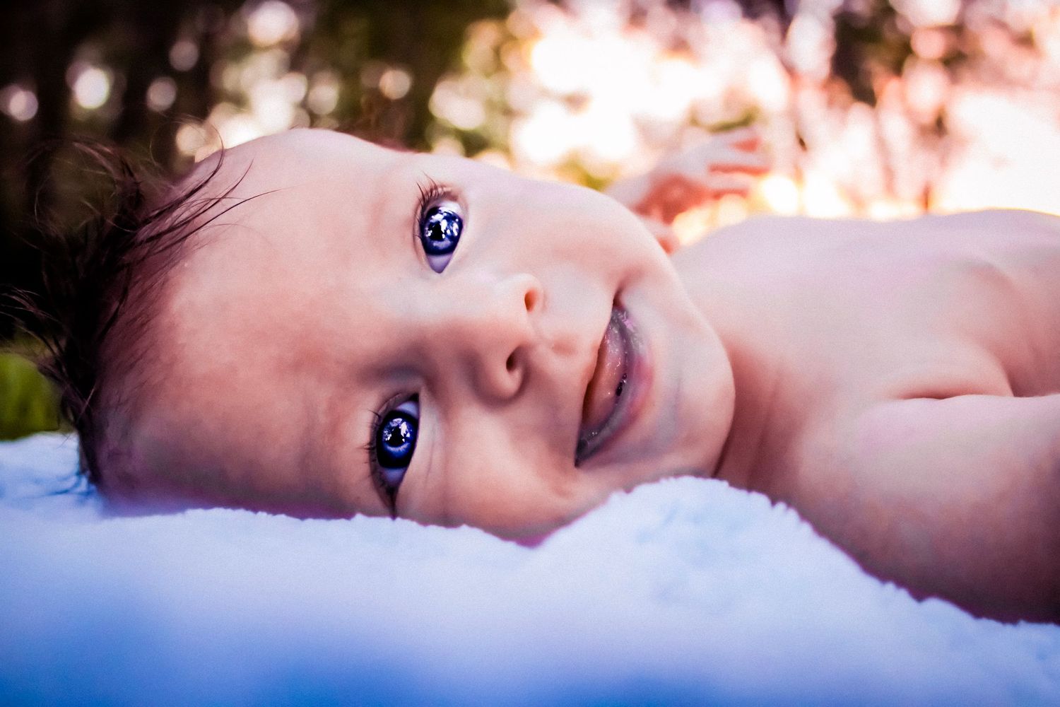 A newborn baby boy smiling at the camera and sticking his tongue out with the sunset in the background.