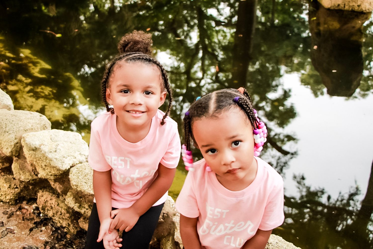 Two girls sitting on a wall with their reflection in the water behind them.