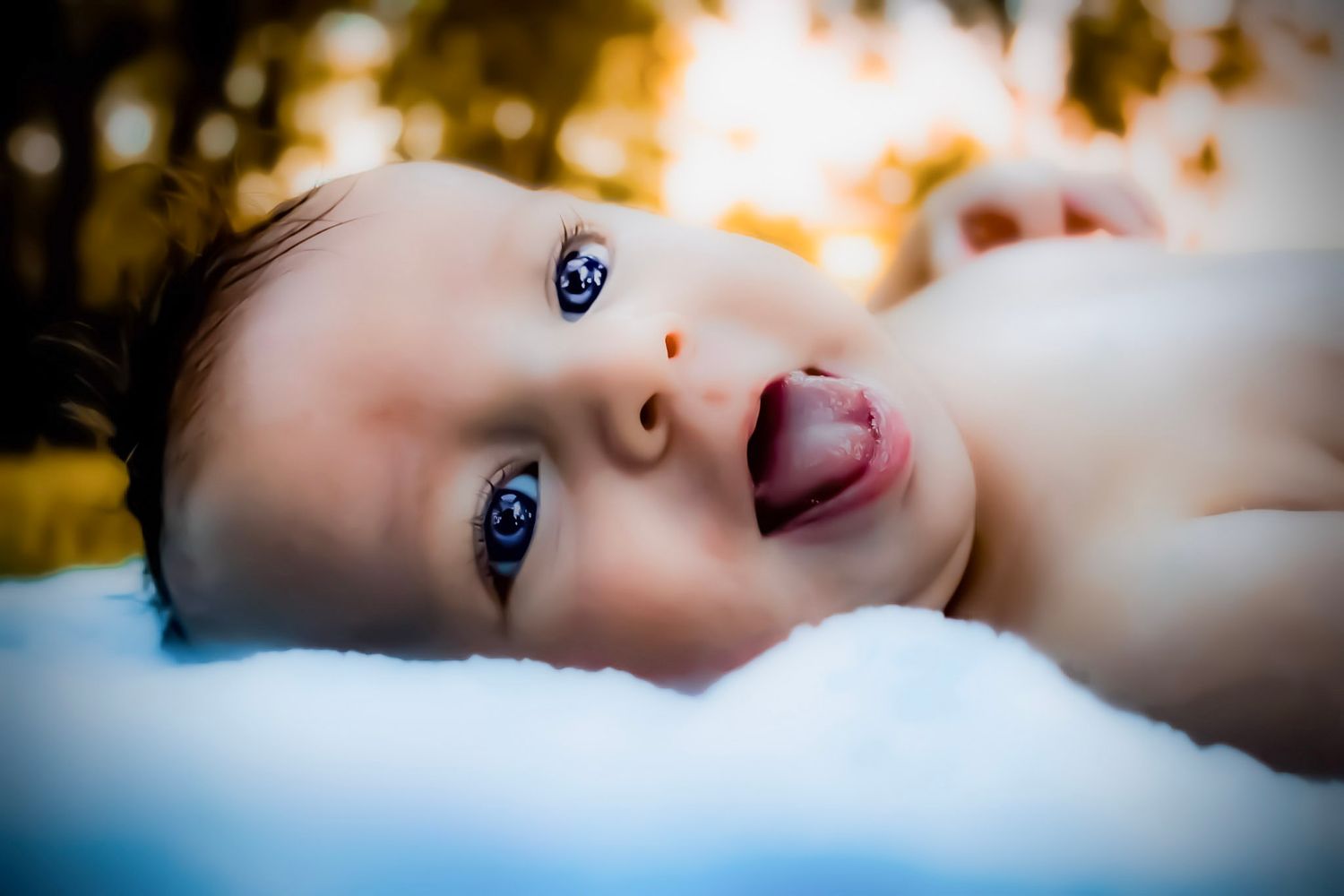 A newborn baby boy with bright blue eyes laying on a blanket outside.