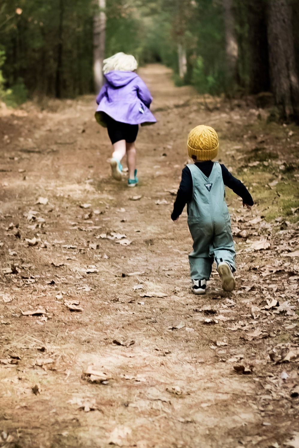 Two children running away from the camera in the woods.