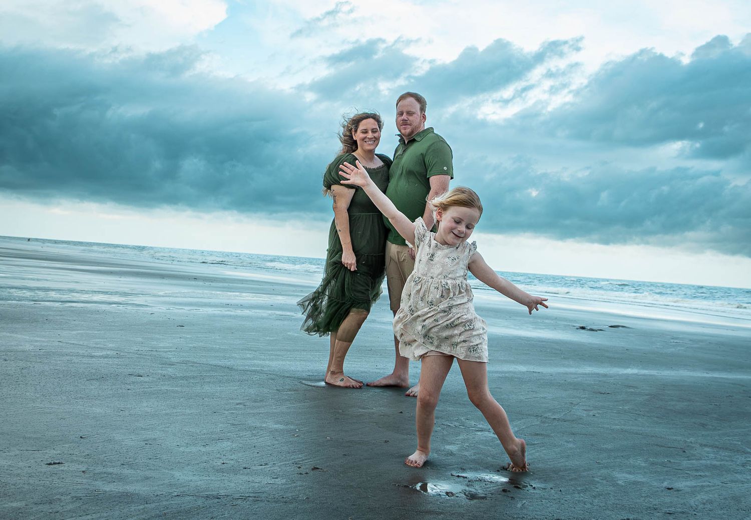 Family of three enjoying a beach day, with a young girl playfully splashing water while parents smile behind her.