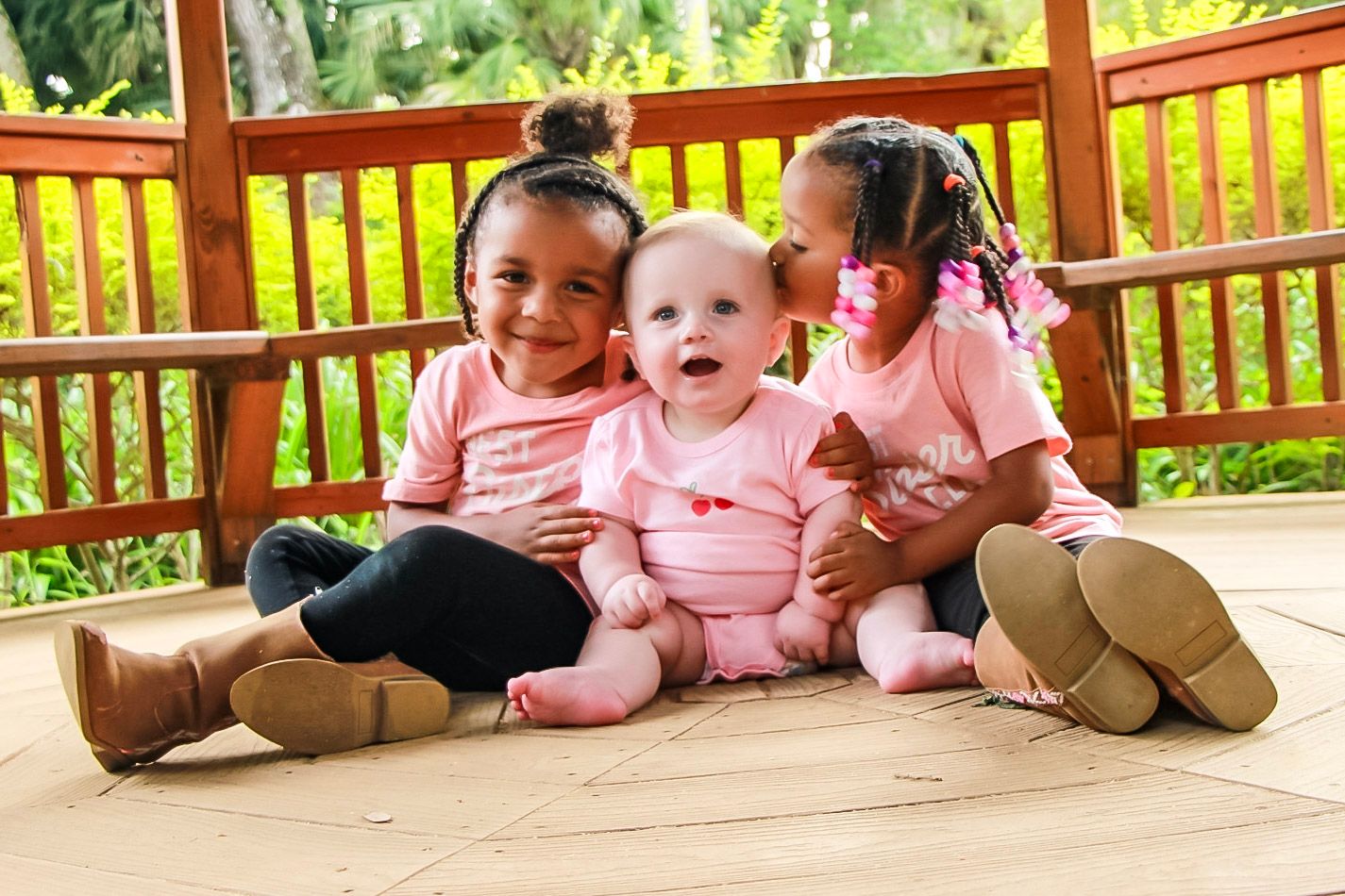 Three siblings sitting in a gazebo. Two are smiling and one his kissing the baby.