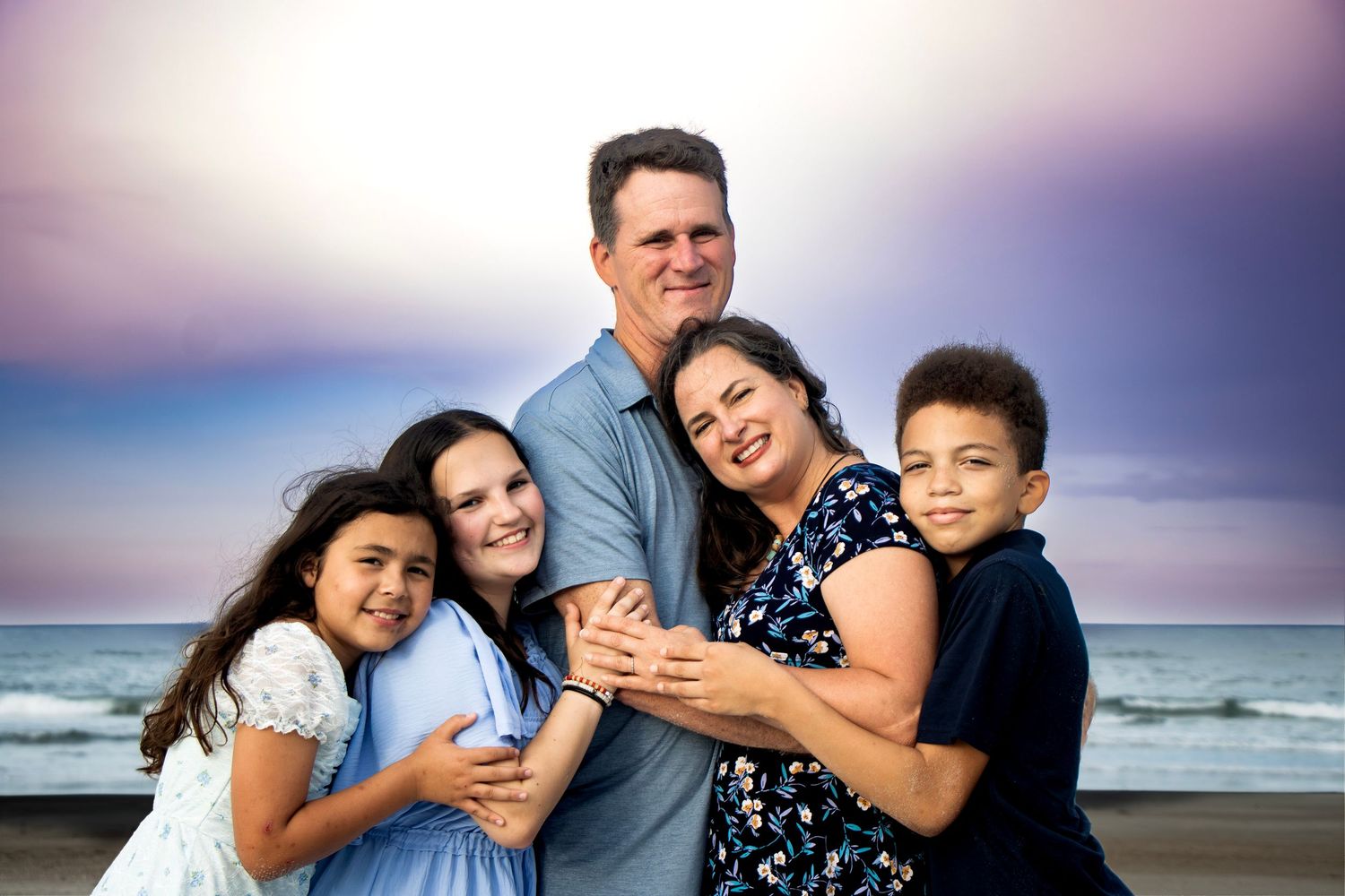 A family of five on the beach in St. Augustine Florida posing for a family portrait with beautiful colors in the sky.