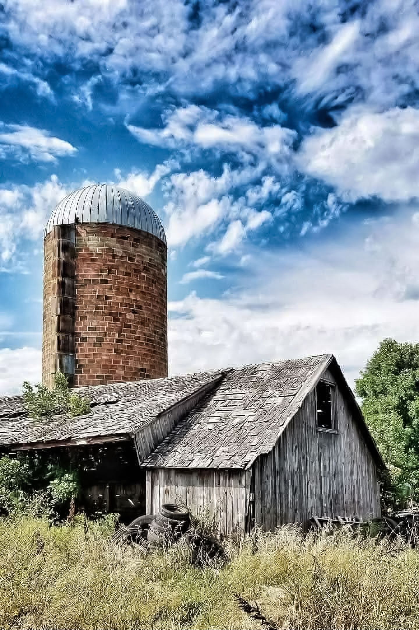 Rustic weather-worn wooden barn falling into ruin along a quiet rural highway under a cloudy sky.