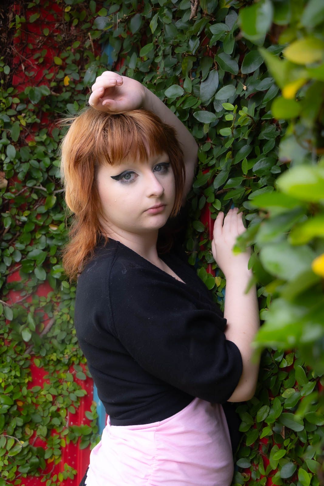 Young woman with dramatic eye makeup posing against lush green ivy wall for a portrait session in Jacksonville, fl.