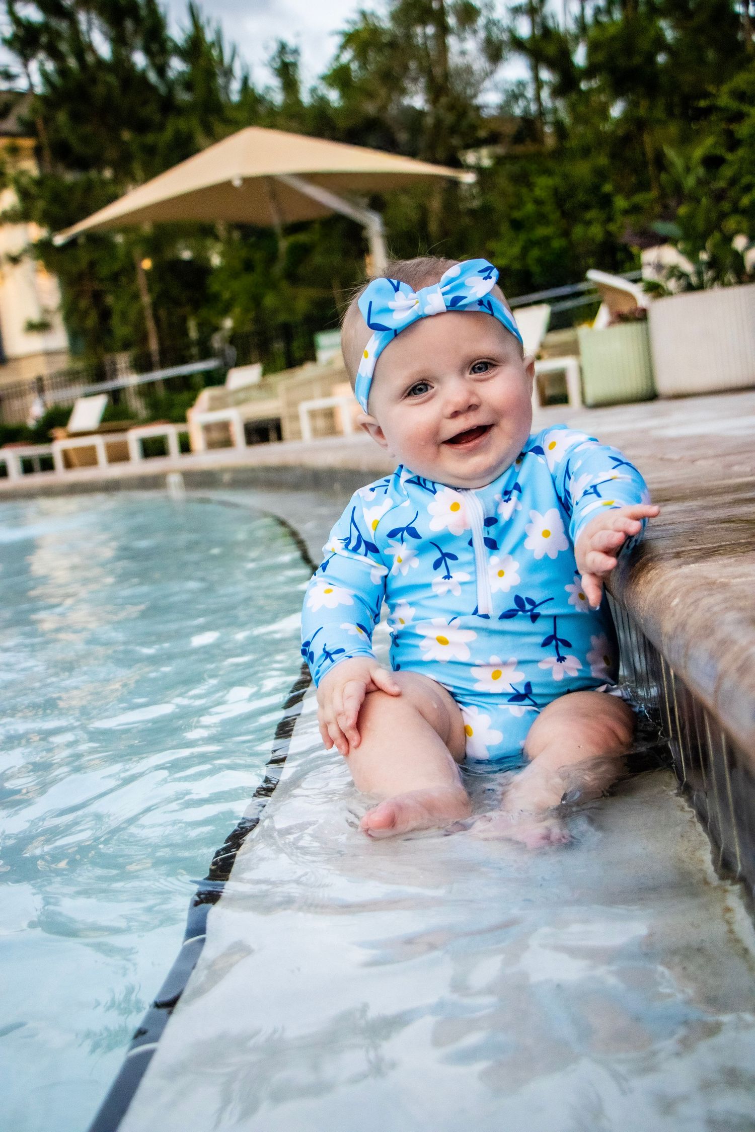 A baby girl sitting in the pool splashing her lets and smiling.
