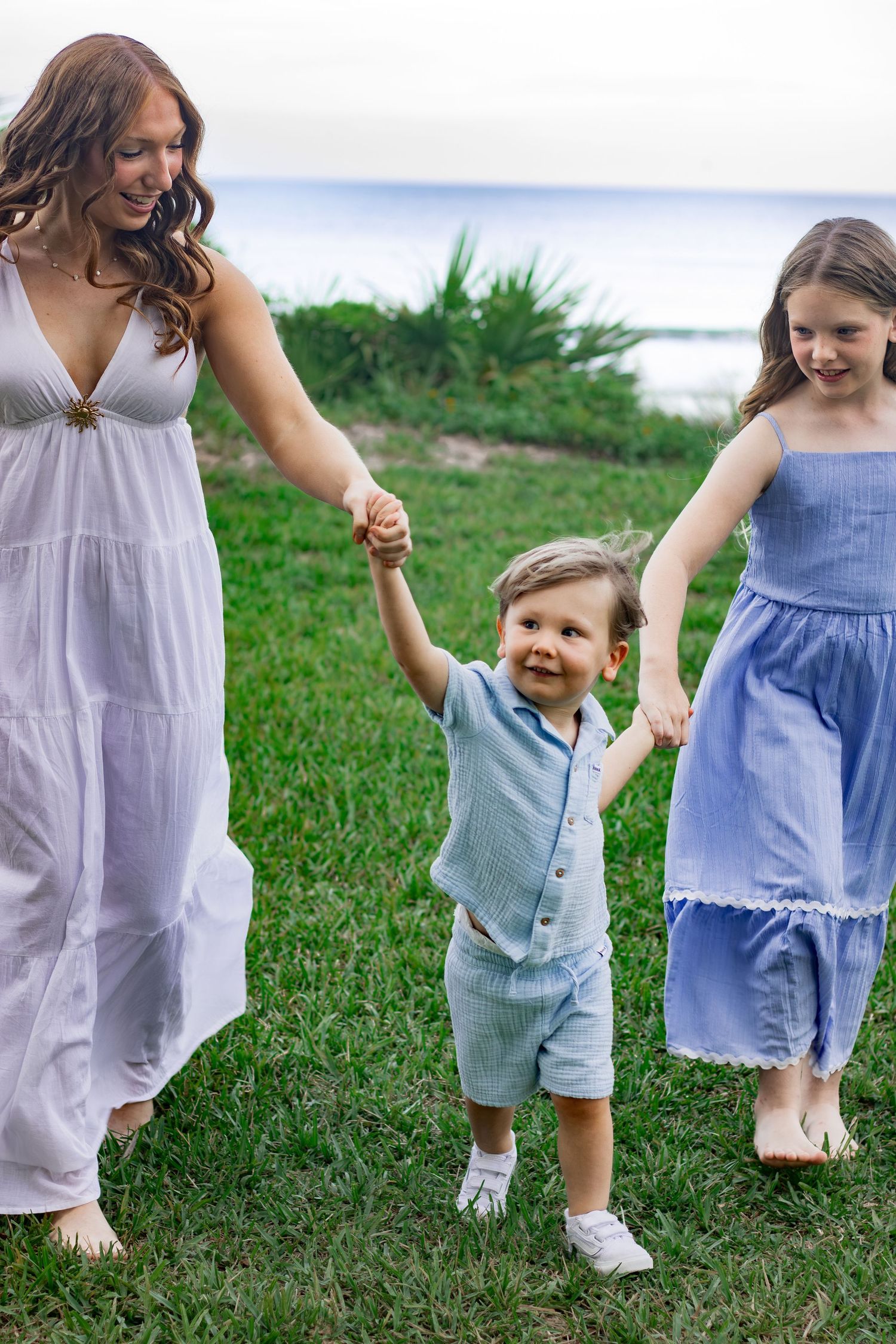 Three children in a milestone portrait holding hands and walking in the grass dancing