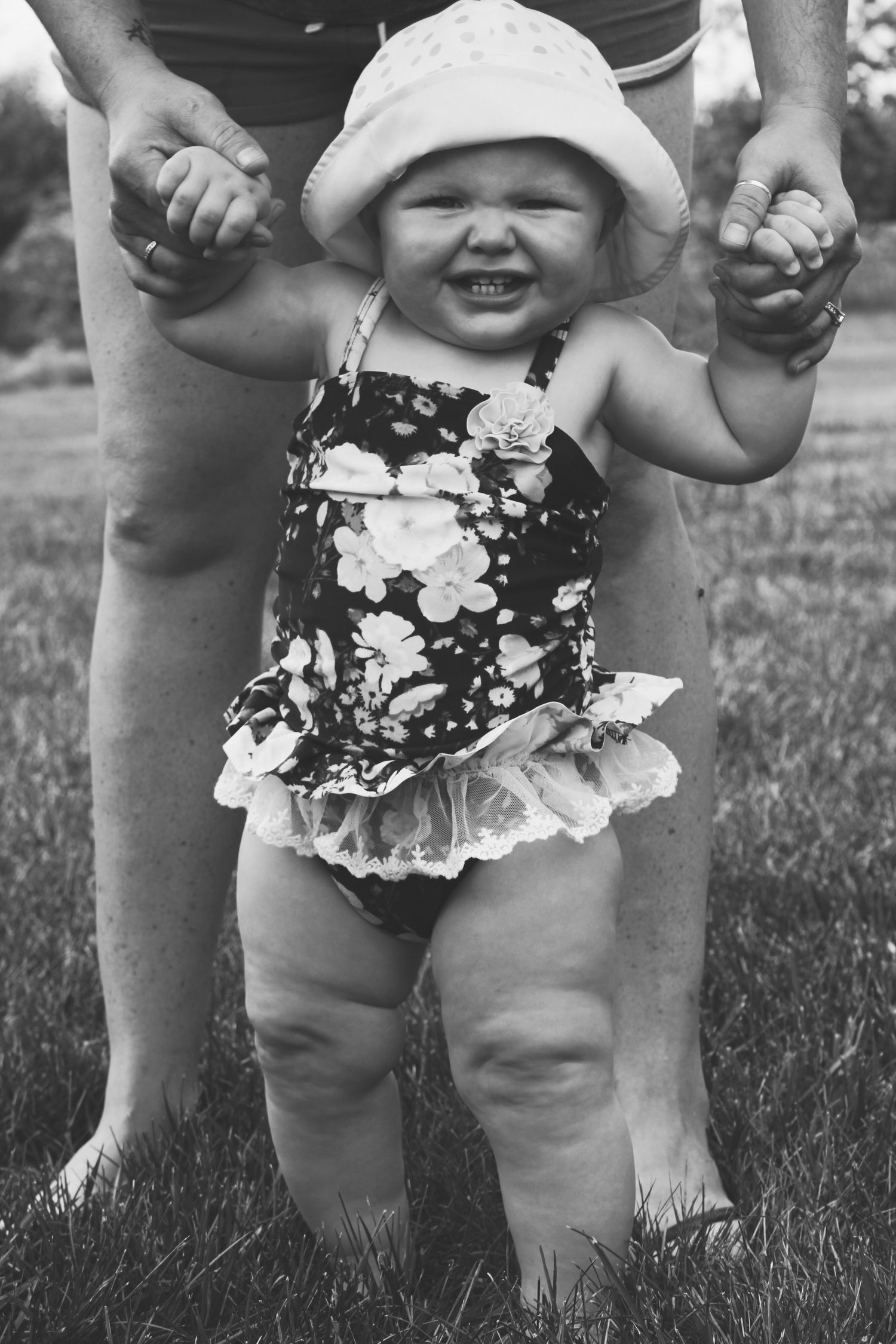 A baby girl wearing a swimming suit being held up for her first steps.