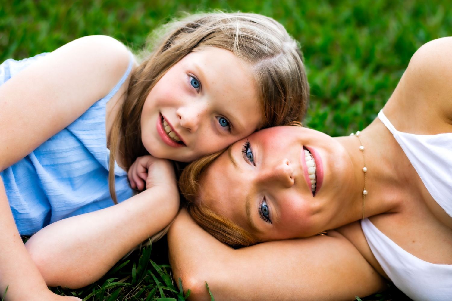 Two sisters laying close to each other touching their temples together while smiling.
