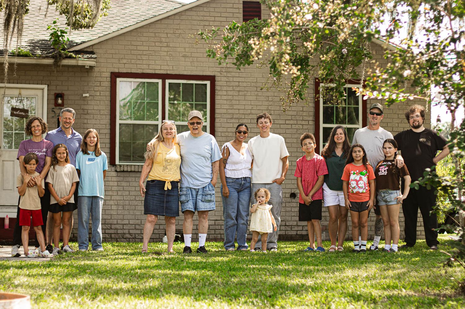 Large family posing together outdoors in front of a brick house on a sunny day for their family portrait session in Florida.