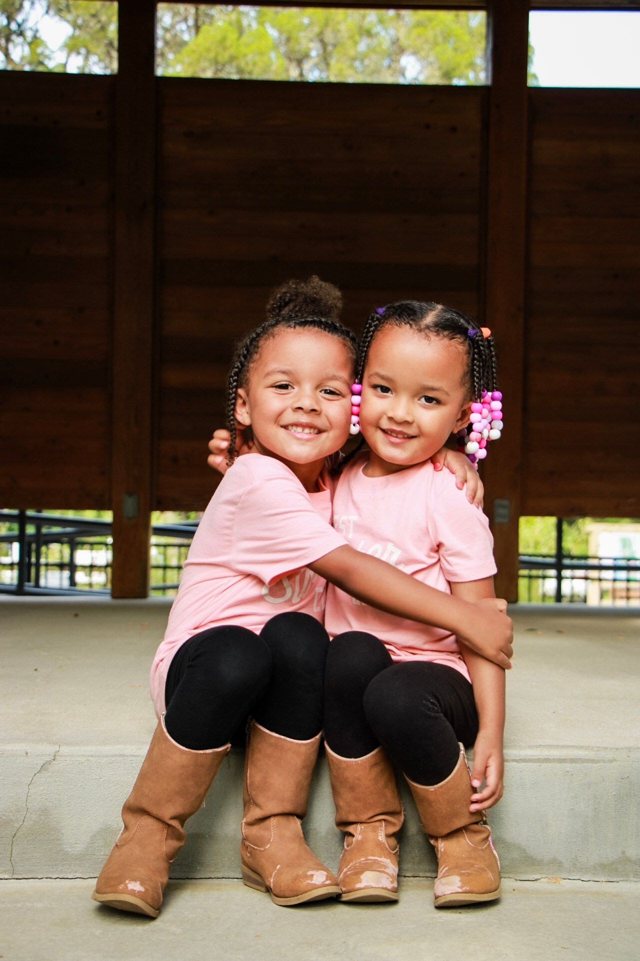 Two toddler girls sitting on steps and hugging each other.