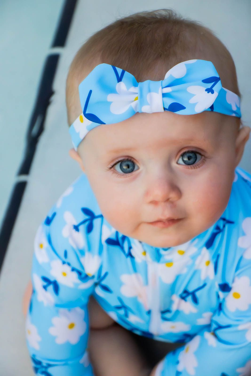 Adorable baby girl with blue eyes wearing a floral blue outfit and matching bow headband.