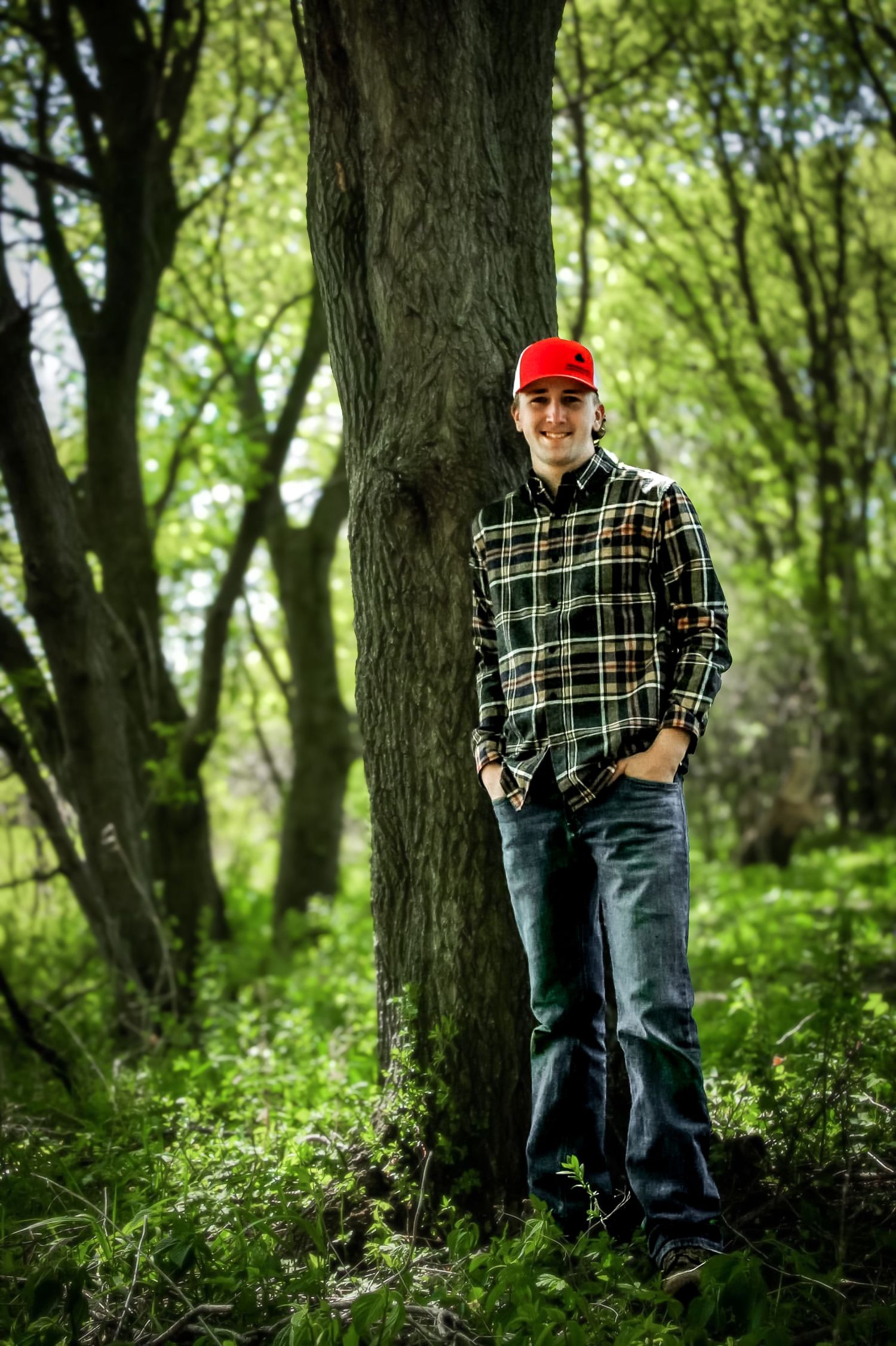 Class senior leaning up against a tree in this beautiful senior portrait wearing a red hat.