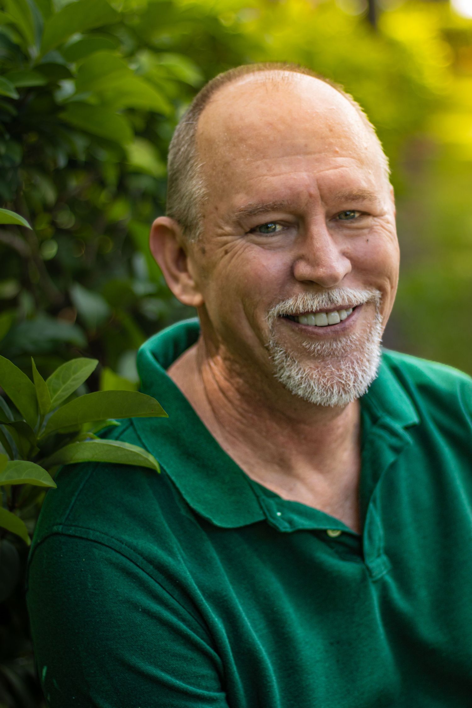 Smiling middle-aged man with mustache wearing green polo shirt among lush green foliage in Fruit Cove, Florida during a branding session.