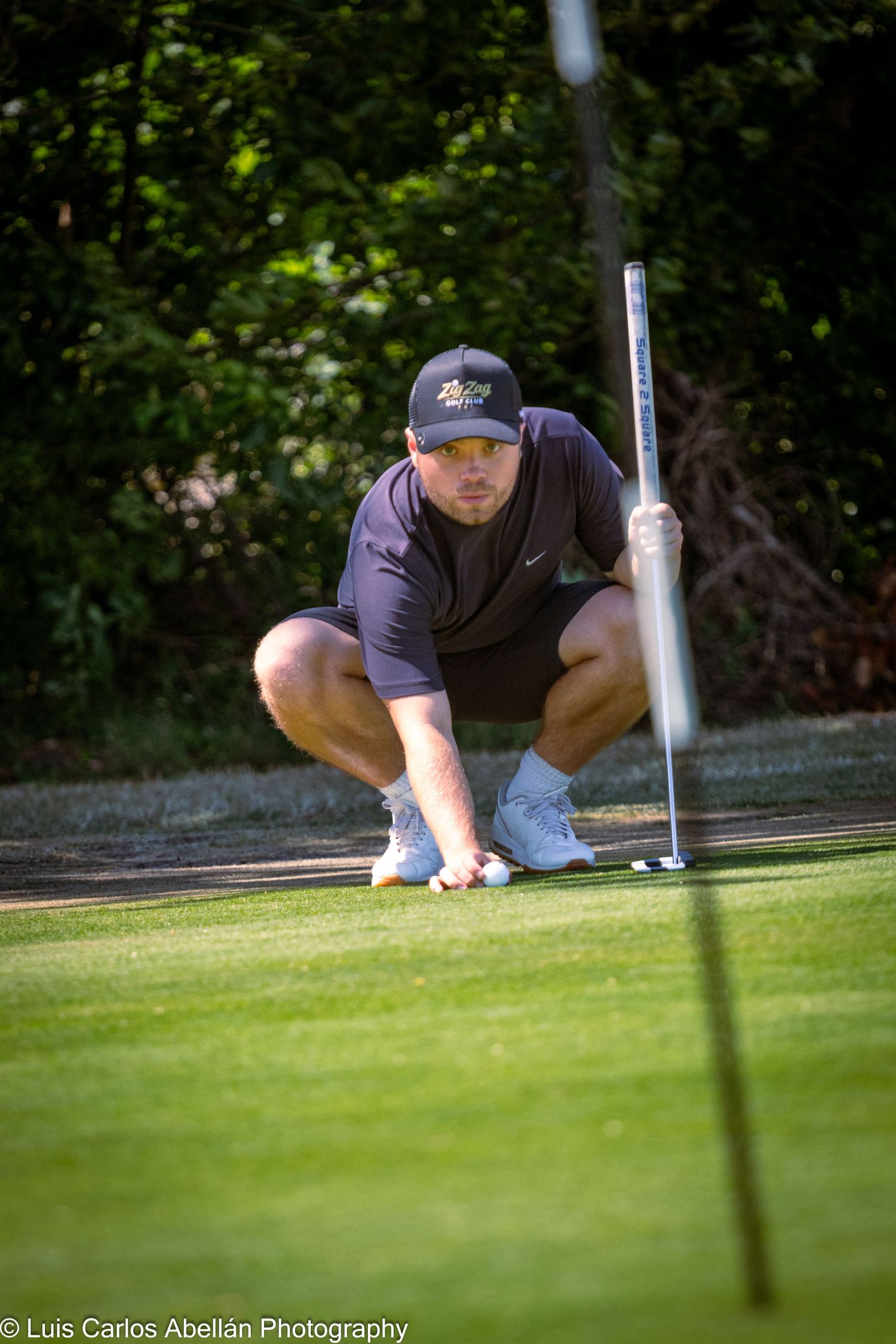 A golfer crouching on a green lined with trees to read the break before a putt during a golf tournament in Kent.